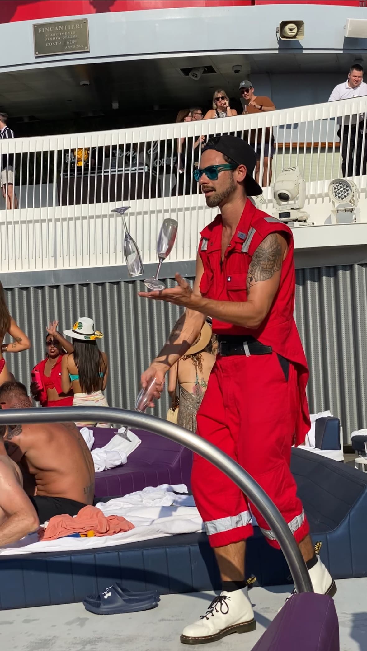 Man in red outfit juggling champagne glasses by the pool area