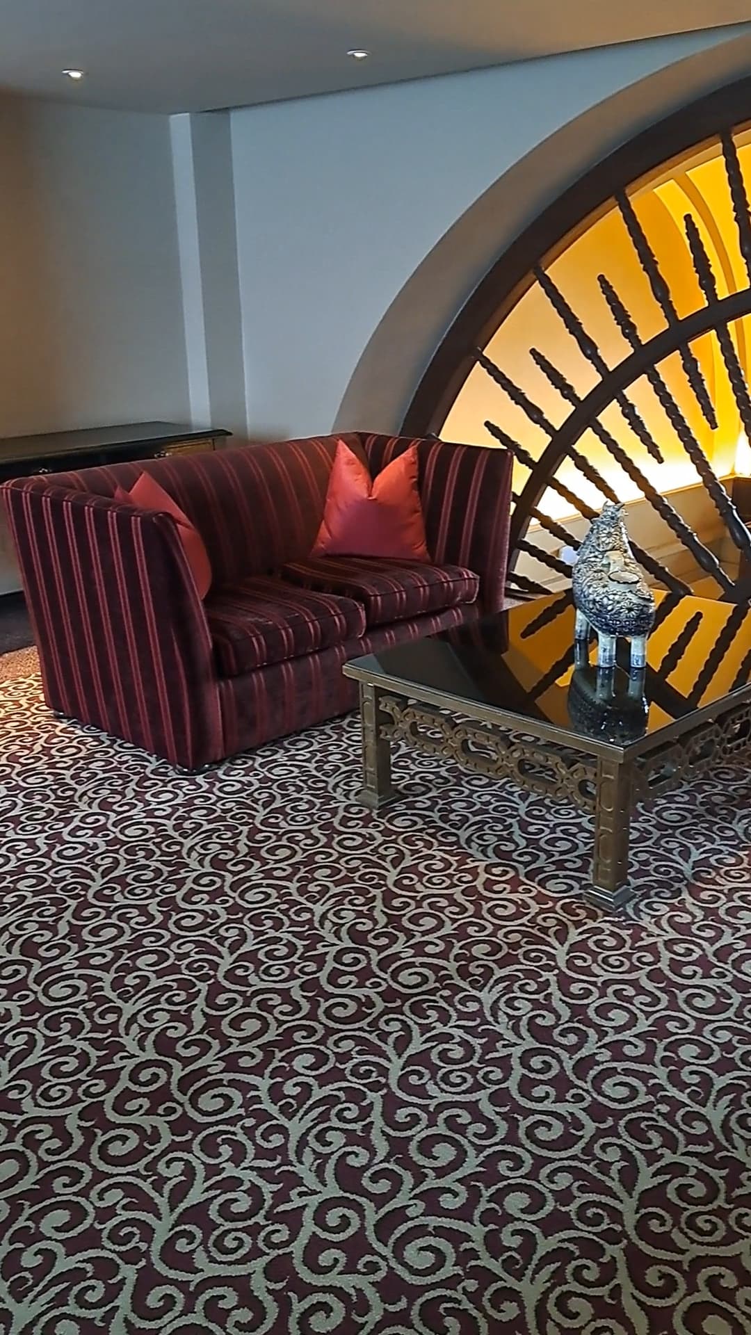 Lounge area in hotel with plush striped sofa and patterned rug next to a large window