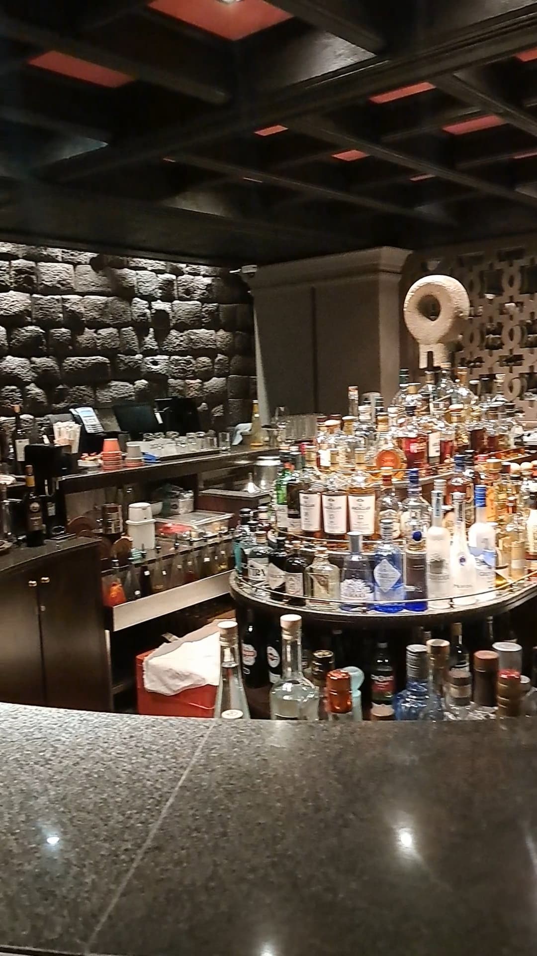 Hotel bar with many different liquor bottles on a central island with gray stone walls in view