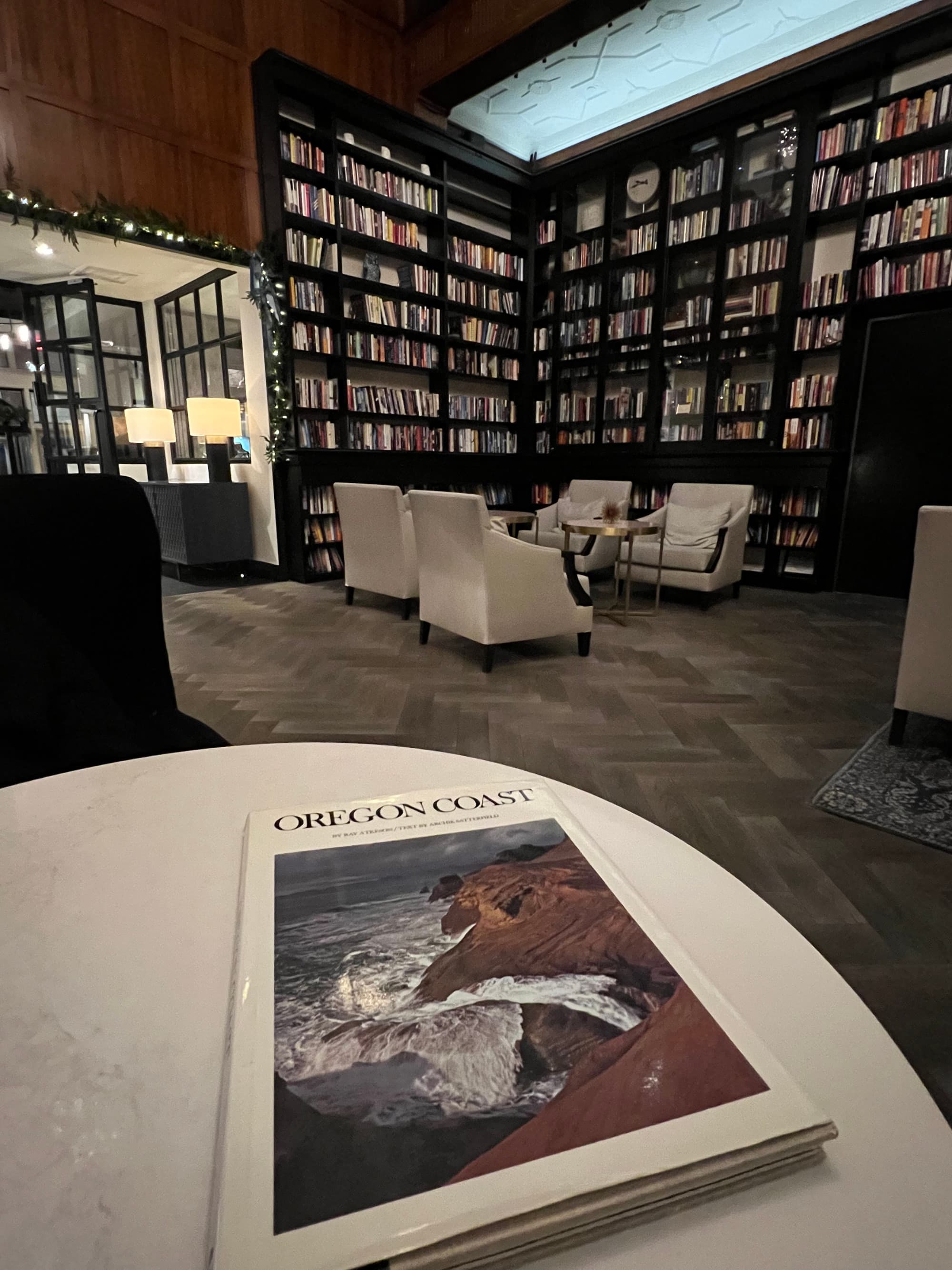 A hotel library with book shelves, white chairs and a round white table with a book on top of it.