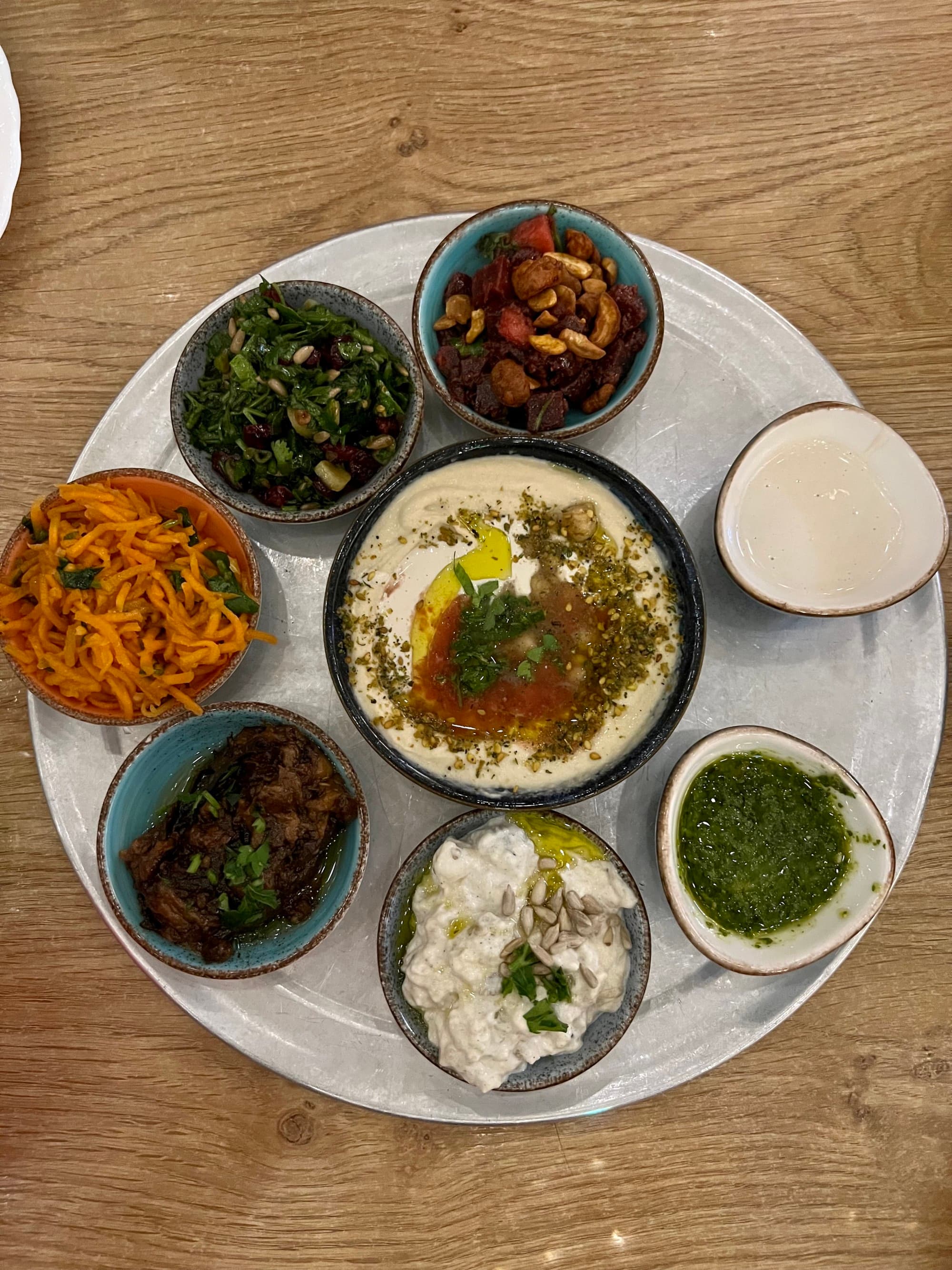 A view of a dip in a bowl with six smaller bowls of toppings and sauces surrounding it.