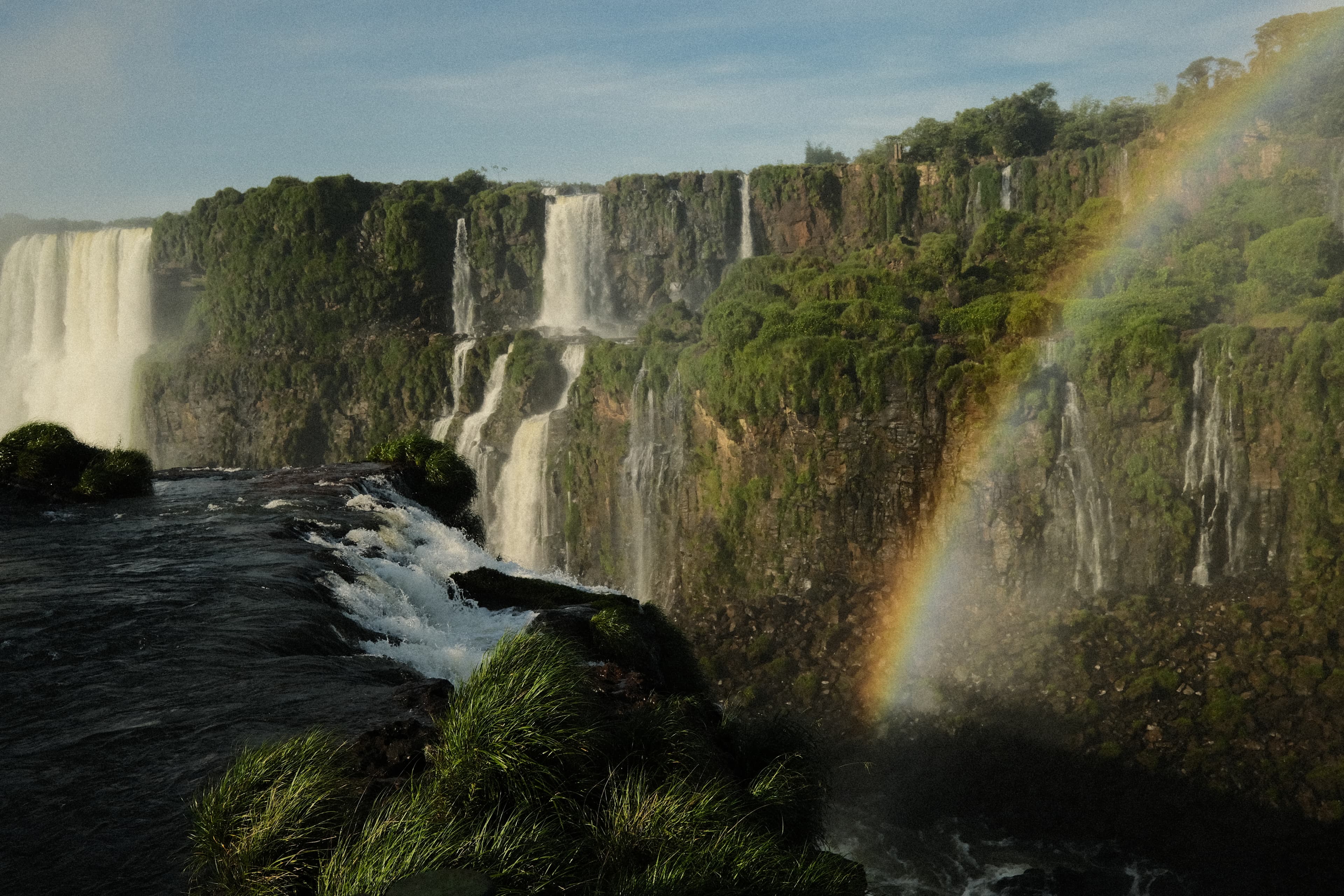 A beautiful lush and green waterfall next to a rainbow.