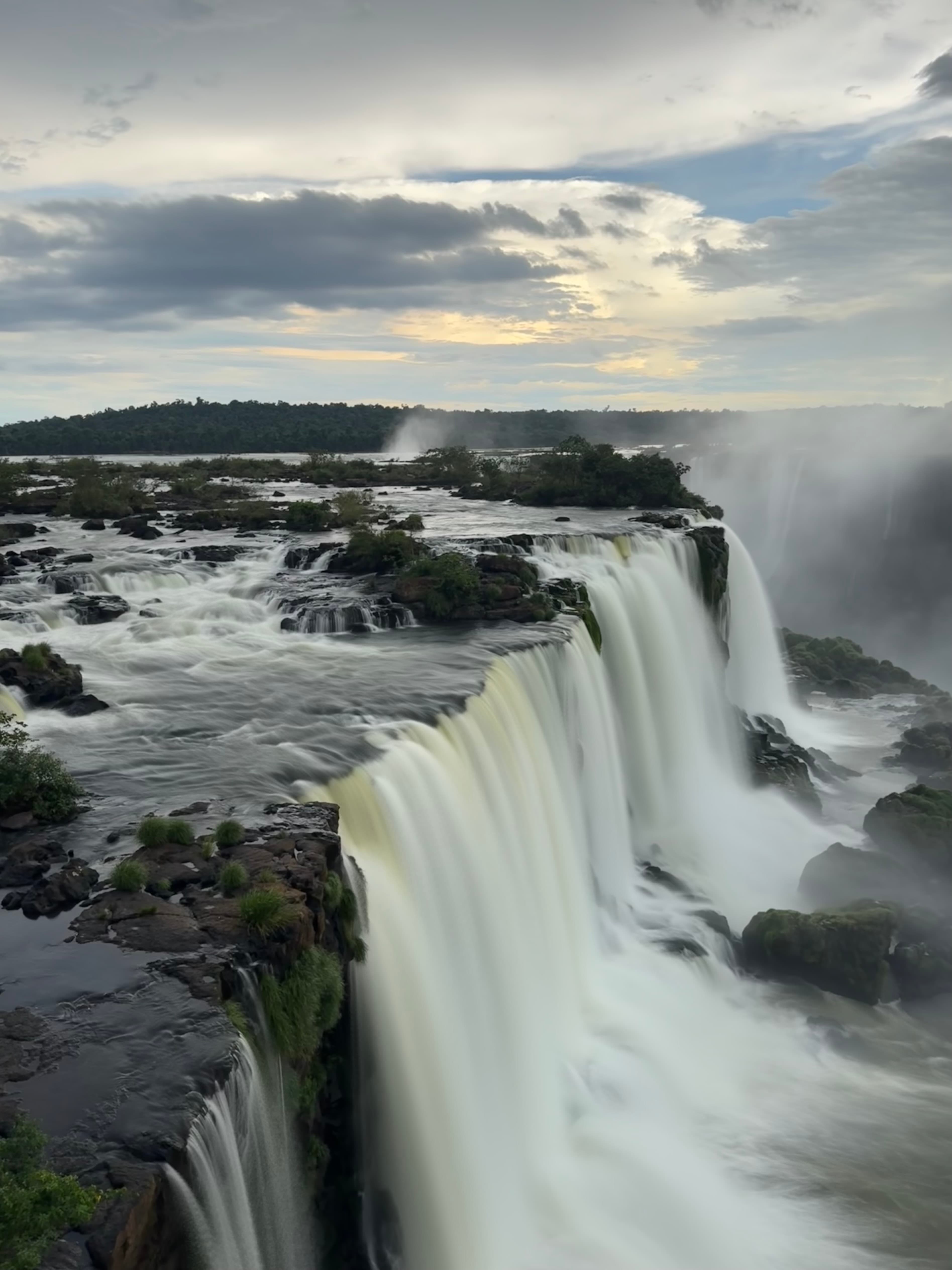 A waterfall and rocky terrain beneath a cloudy sky.