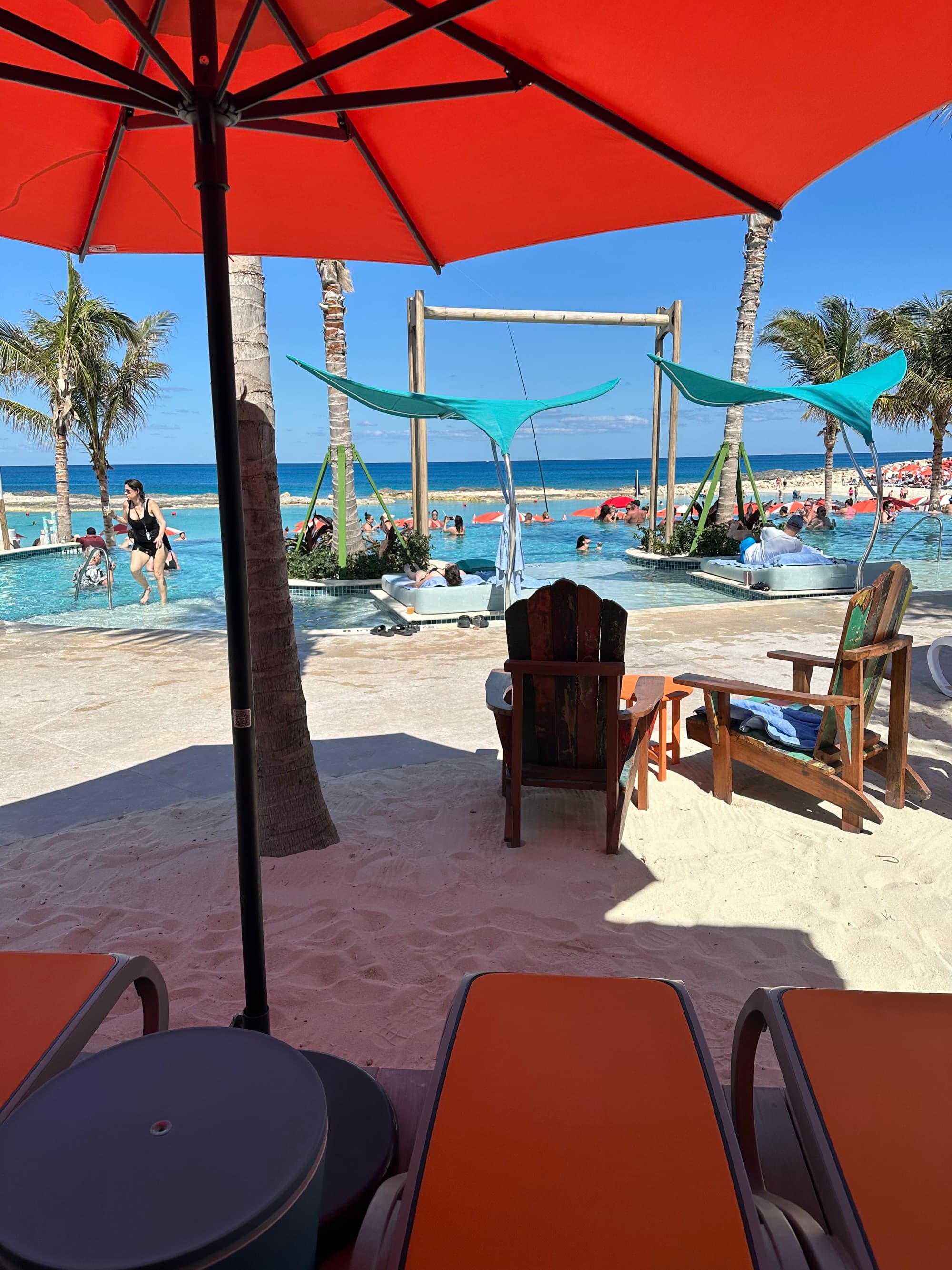 A view of the pool and beach from underneath an orange umbrella