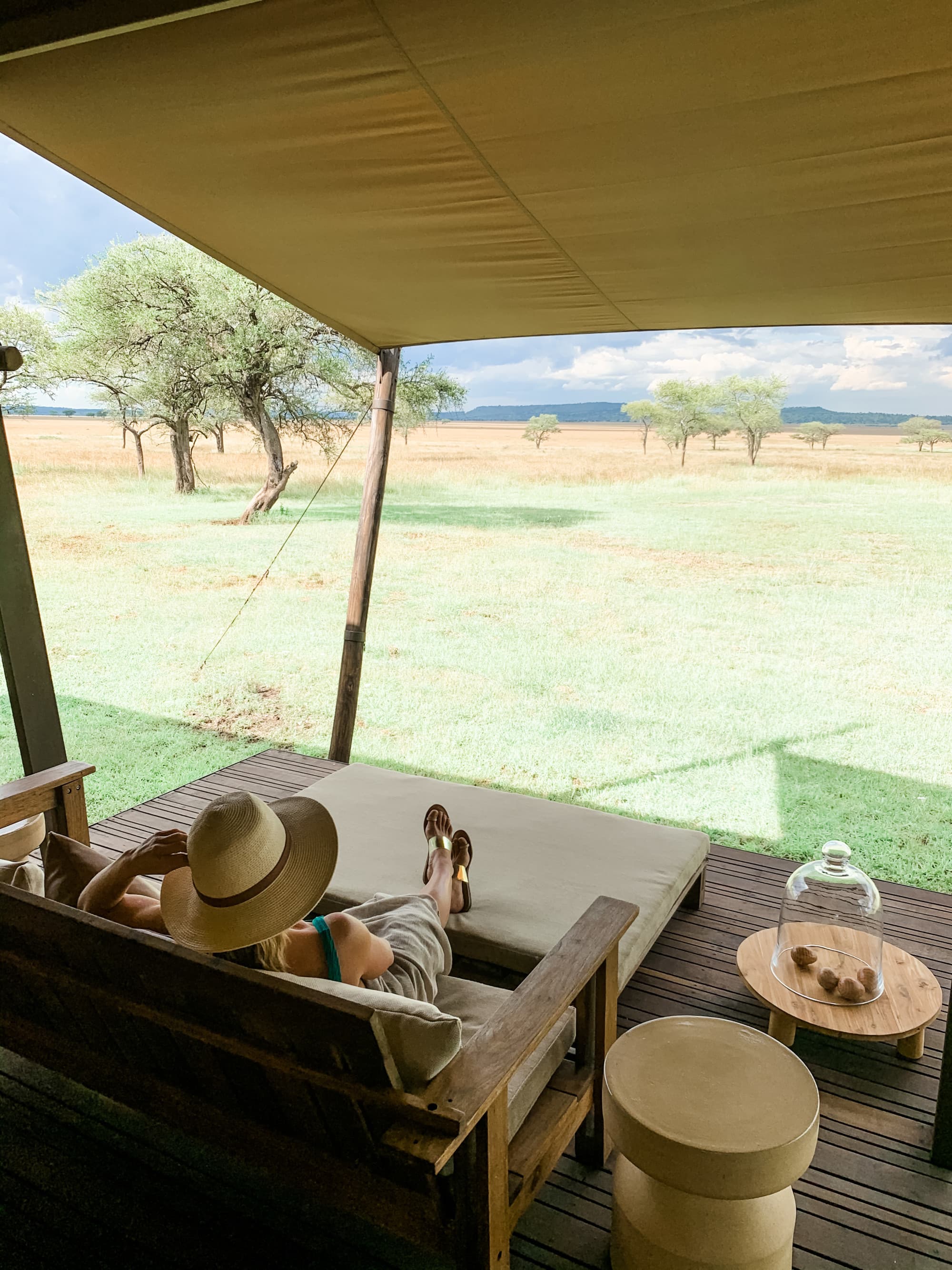 a woman sits on a daybed overlooking a grassy expanse