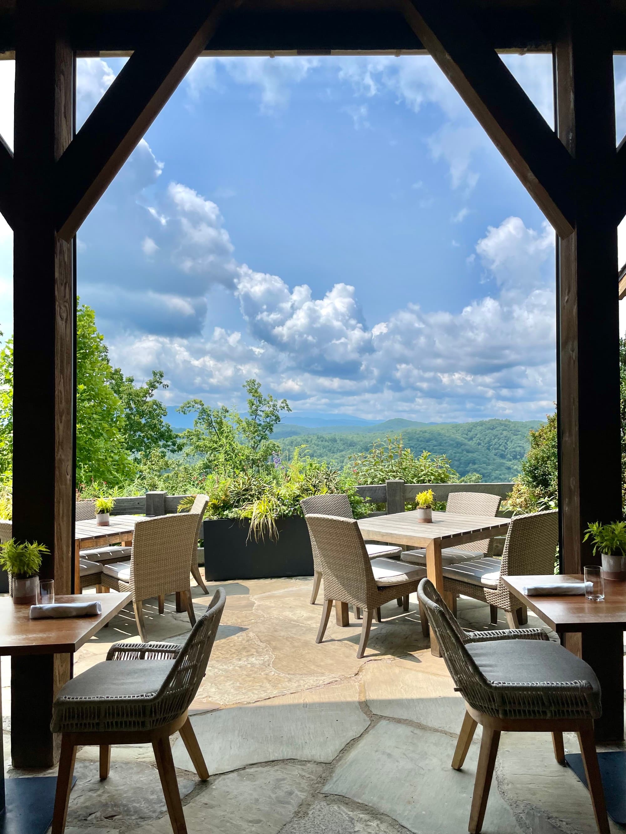 A restaurant patio with dining chairs, a wooden archway and a view of the mountain range in the distance.