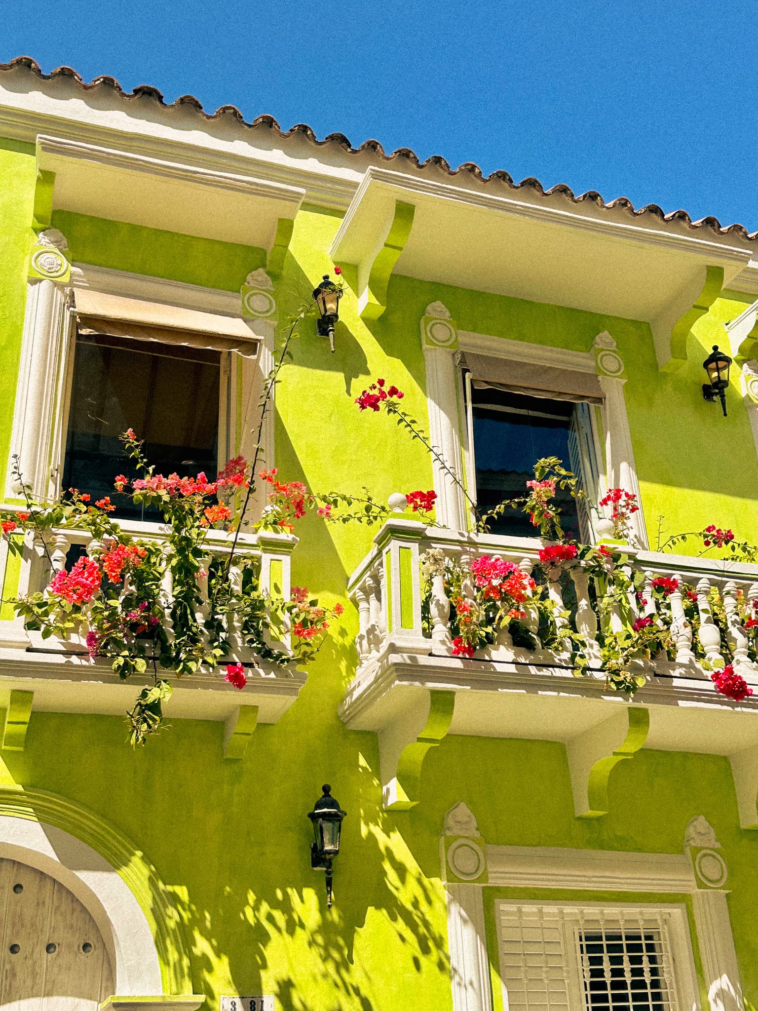 A beautiful lime green building with white balconies, red flowers and a terracotta roof.