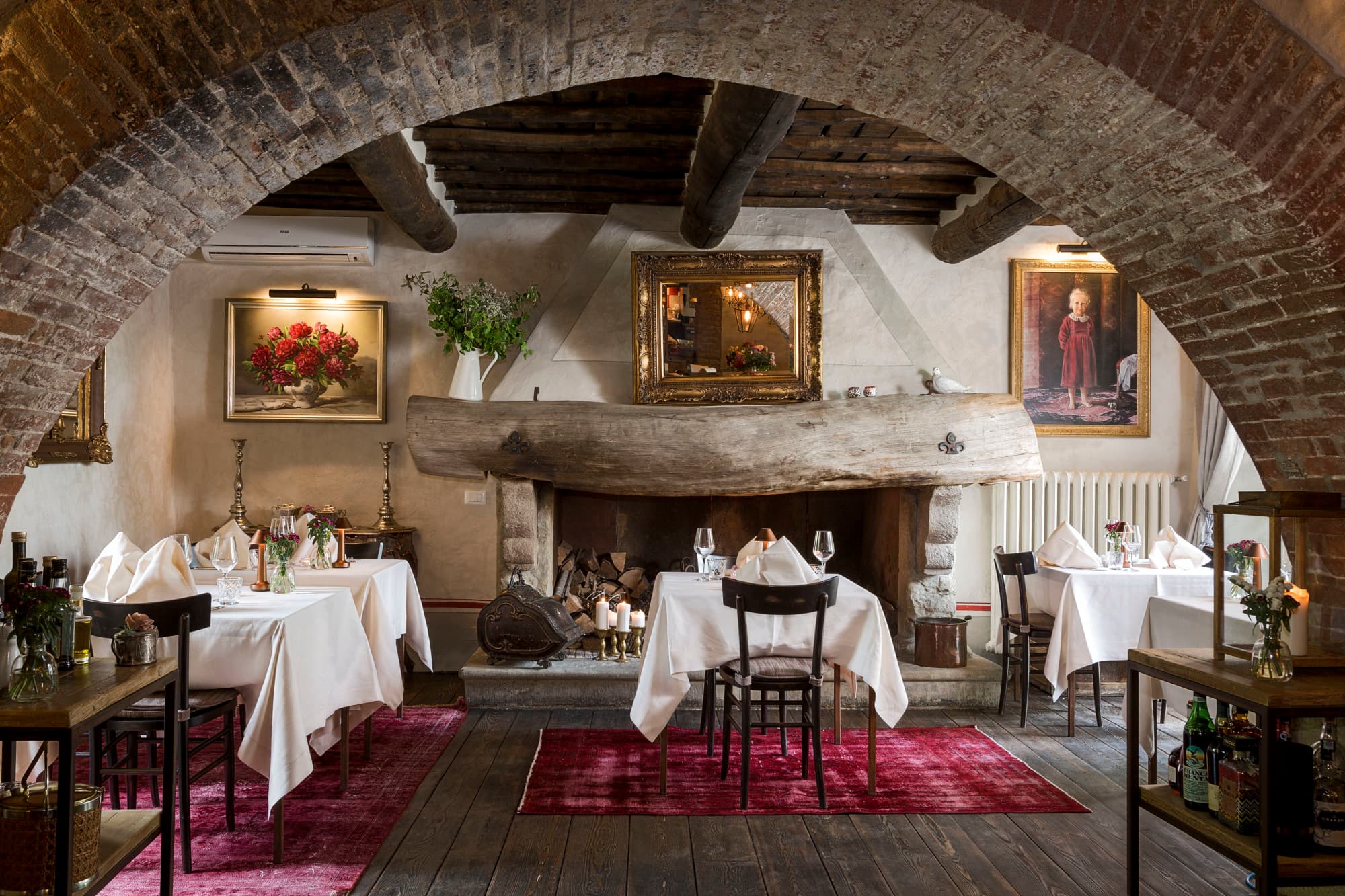 tables with white tablecloths sit on red rugs beneath a large brick archway