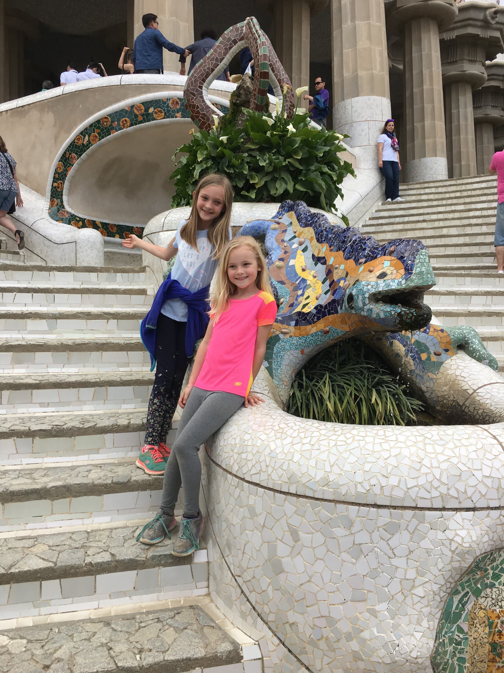 Two children posing on stone steps next to a mosaic tiled lizard water feature.
