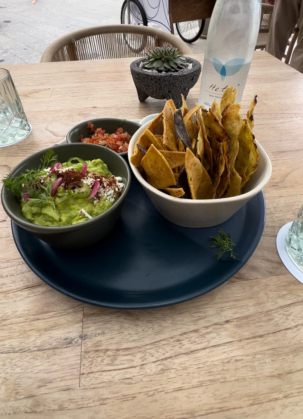 A plate full of chips and guacamole on top of a wooden table with a carafe of water in the background.