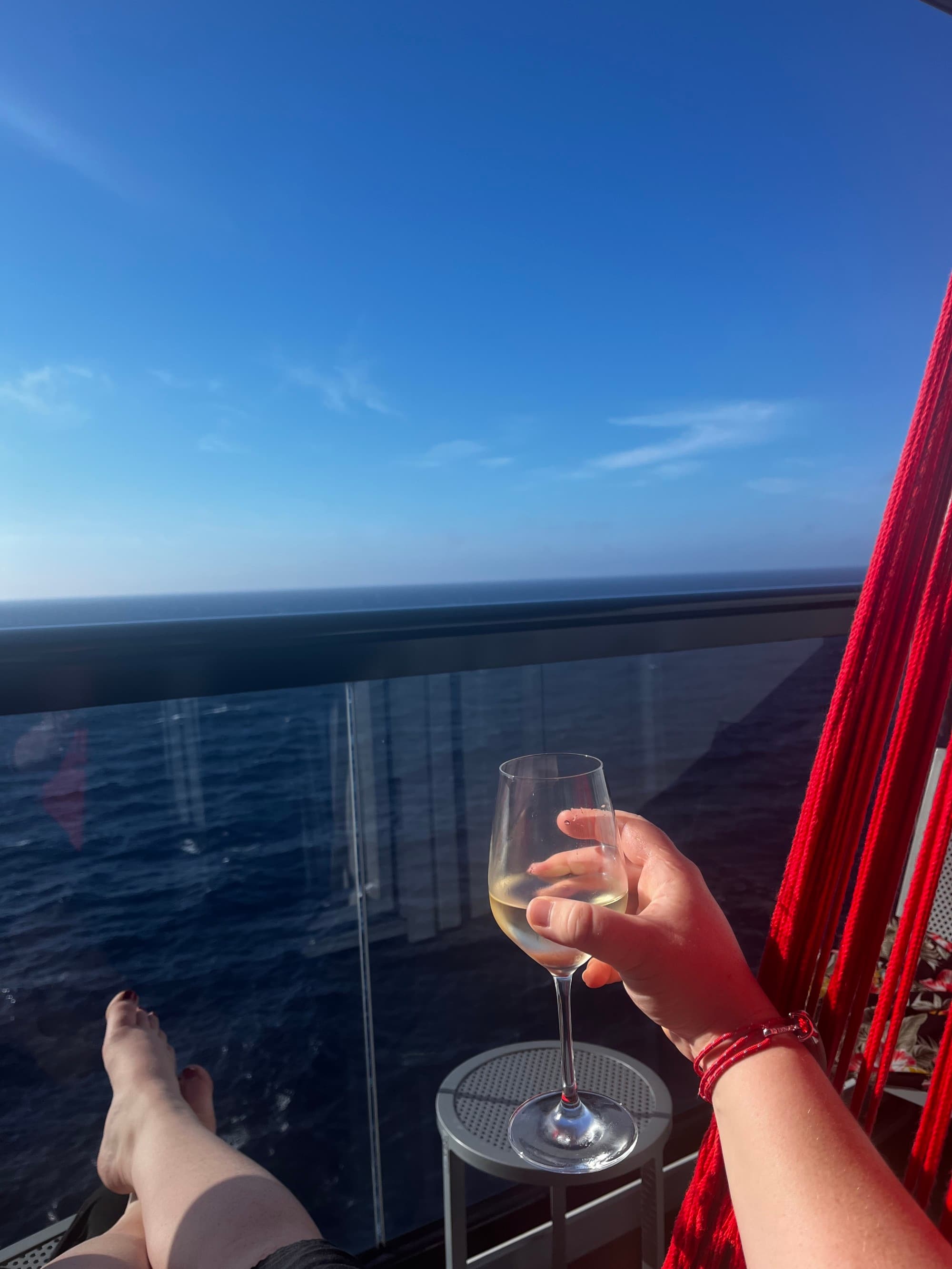 A person holding a glass of wine in front of a balcony view of the ocean