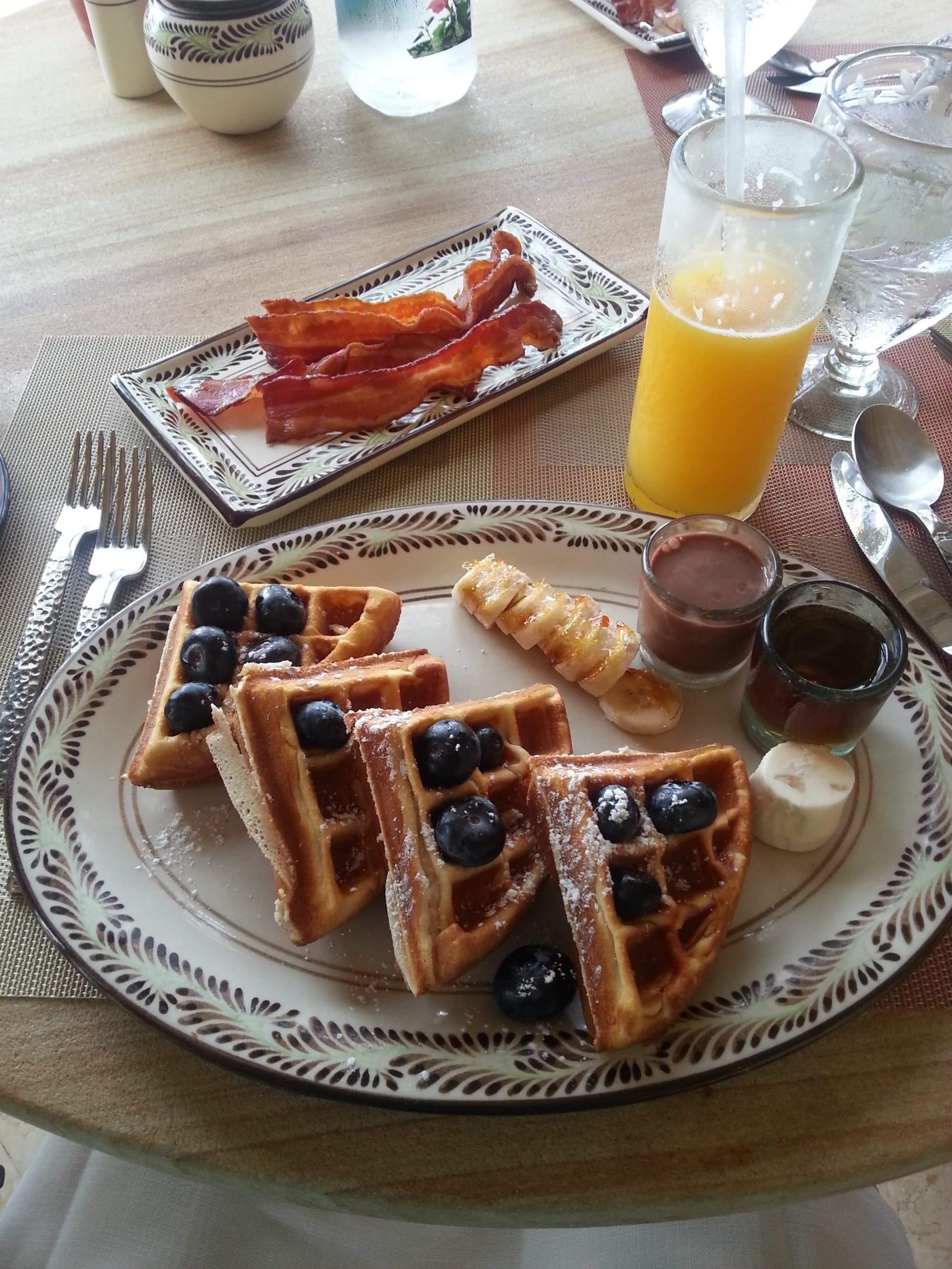 Plates of breakfast food on a table with a glass of orange juice