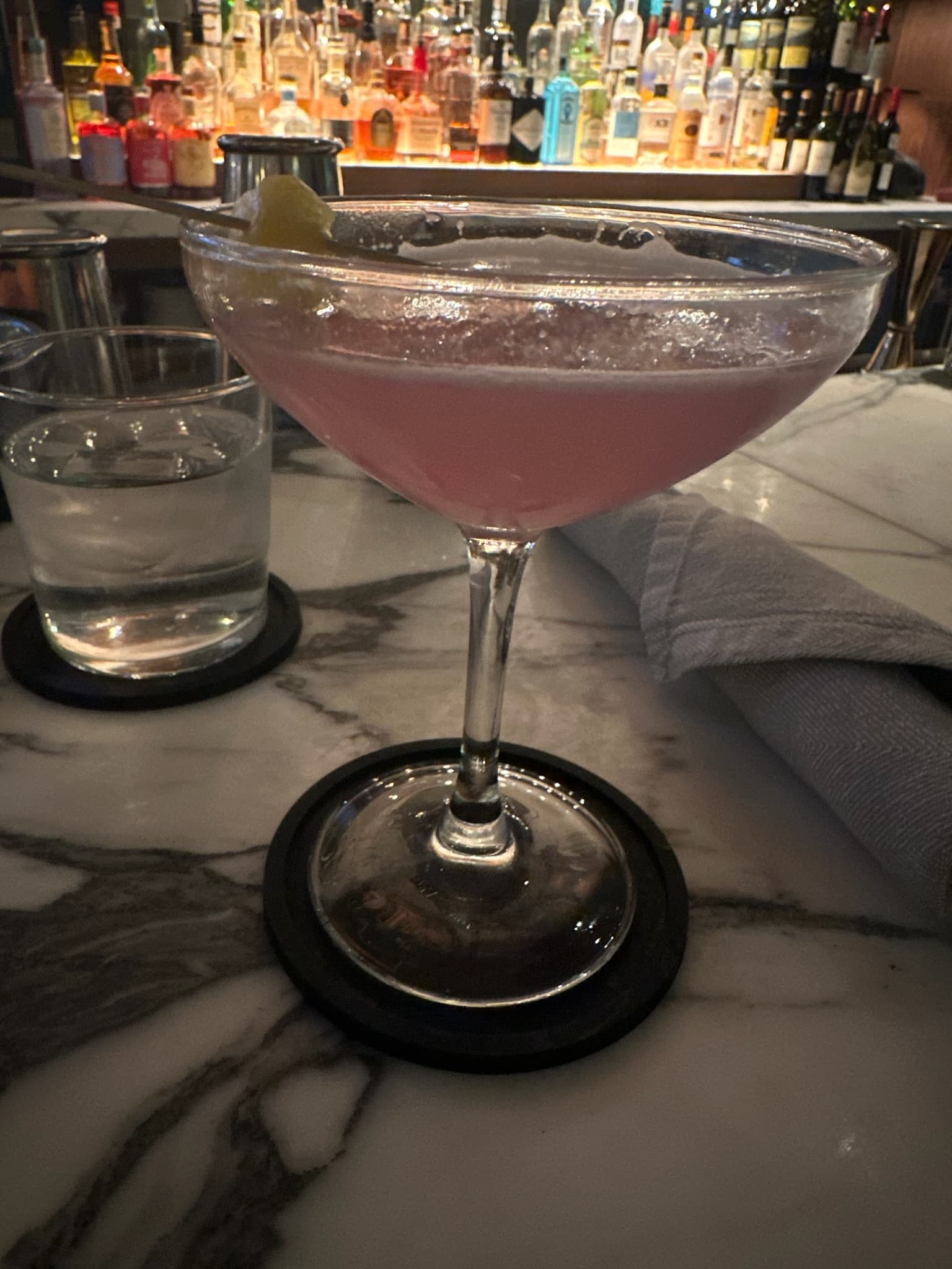 A pink drink in a martini glass sitting on a bar