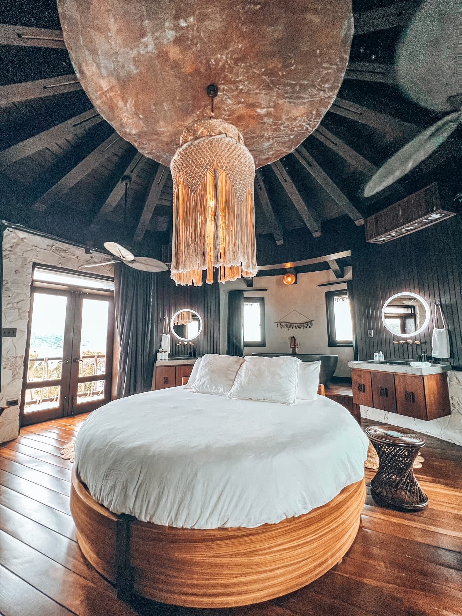 A circular bed with white sheets under a macrame light fixture