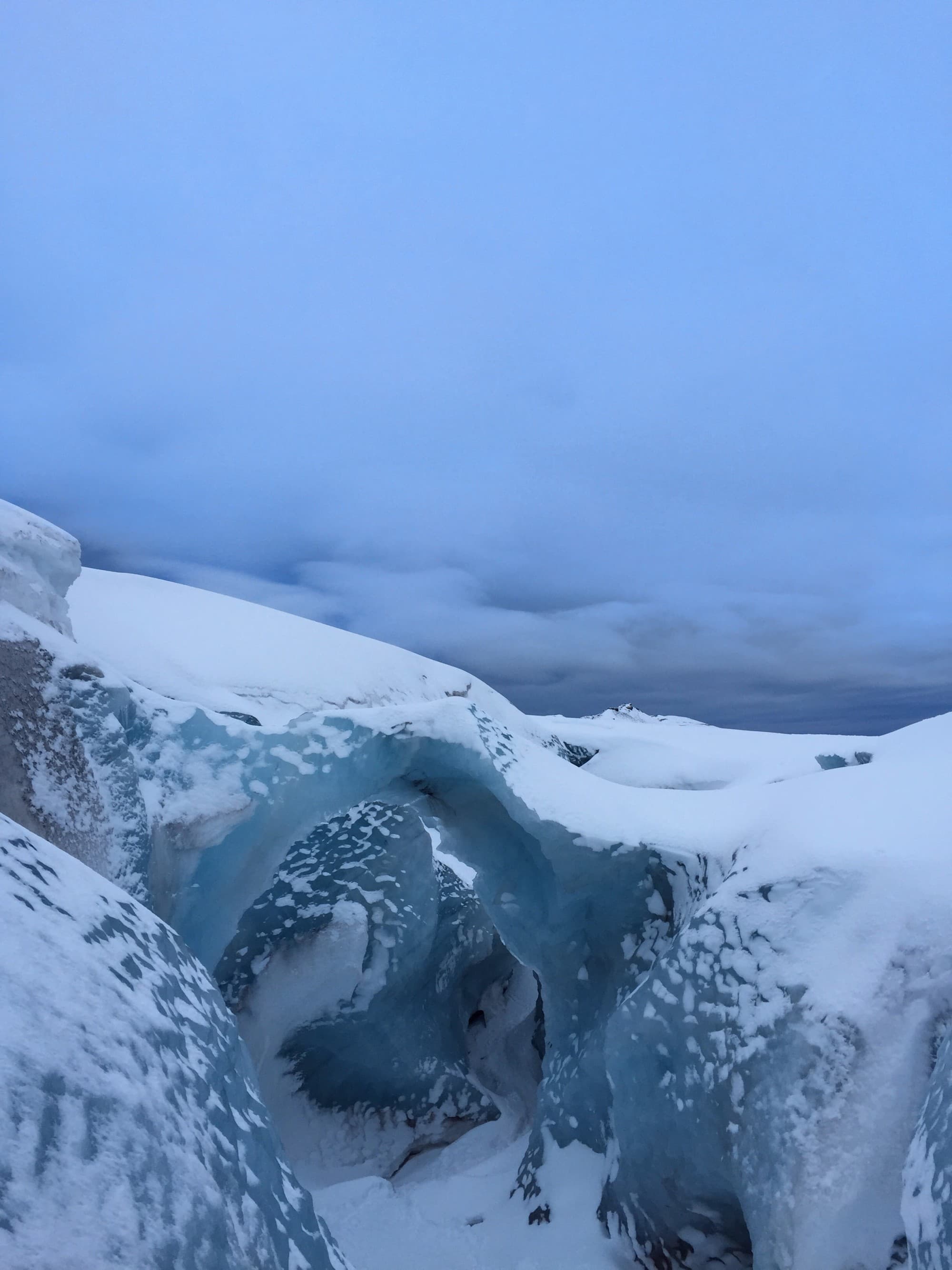A large ice formation surrounded by snow and cloudy skies.