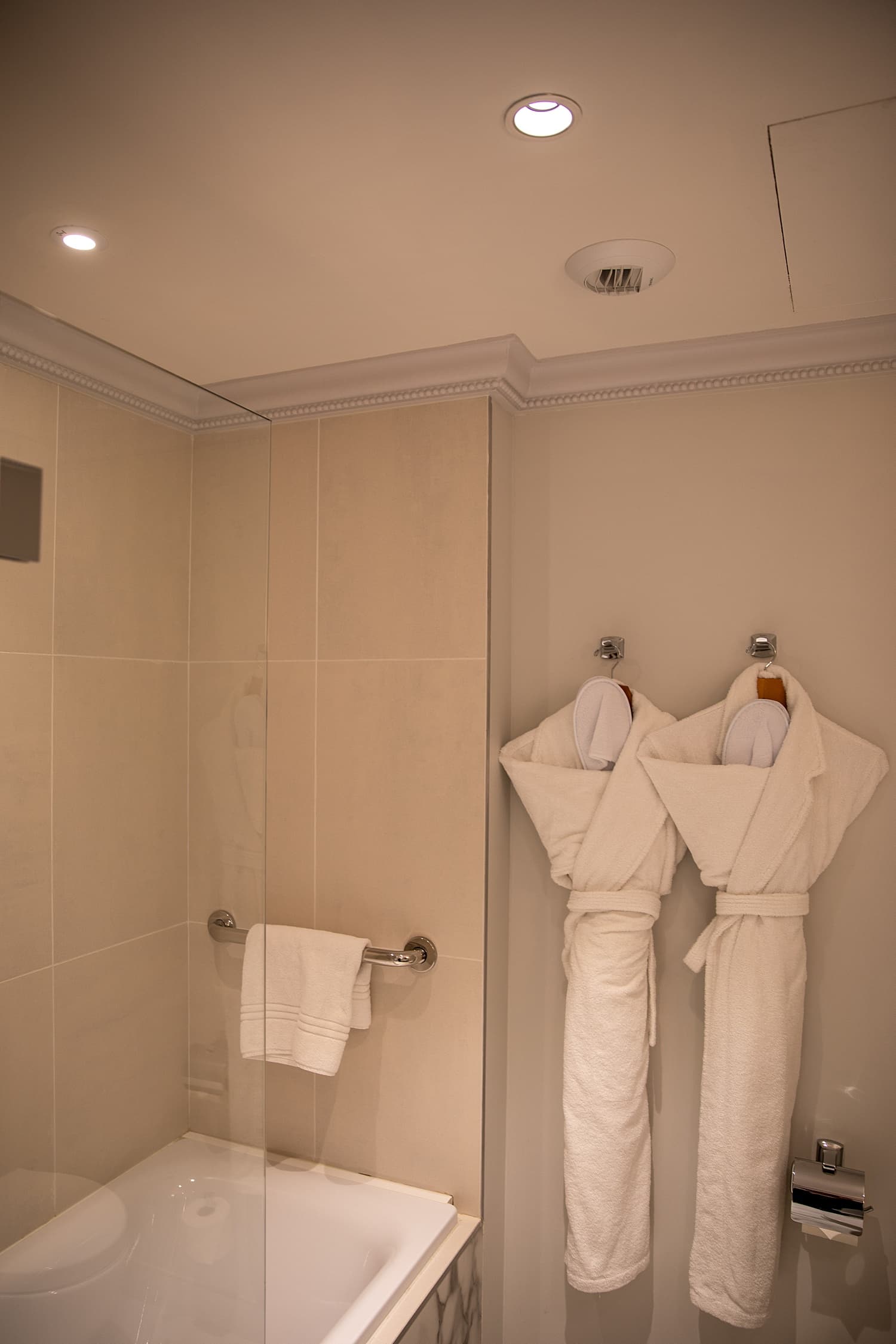 A hotel bathroom with two robes hanging up