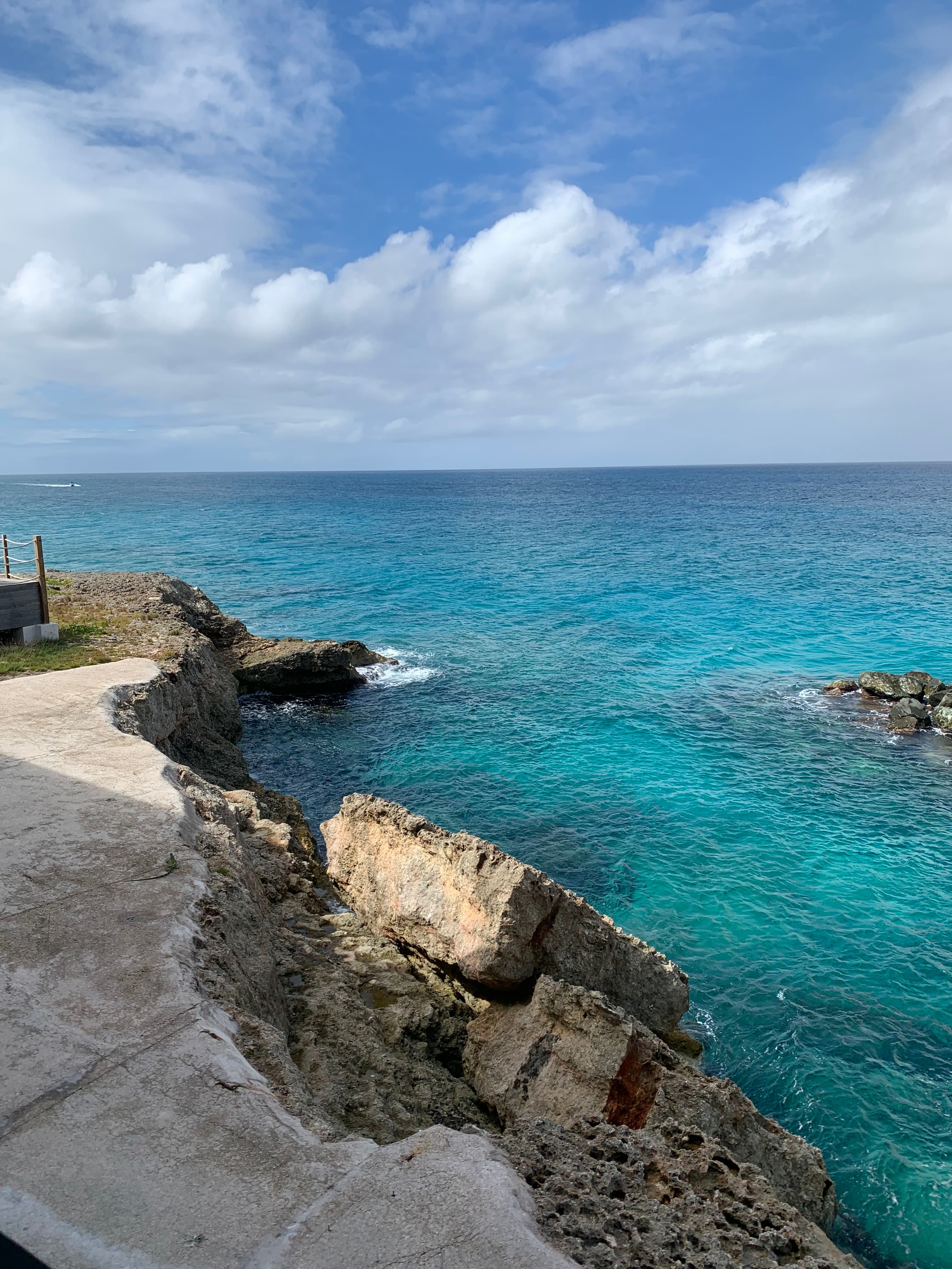 A beautiful view of a rocky cliff leading out to turquoise blue waters beneath the cloudy blue sky.