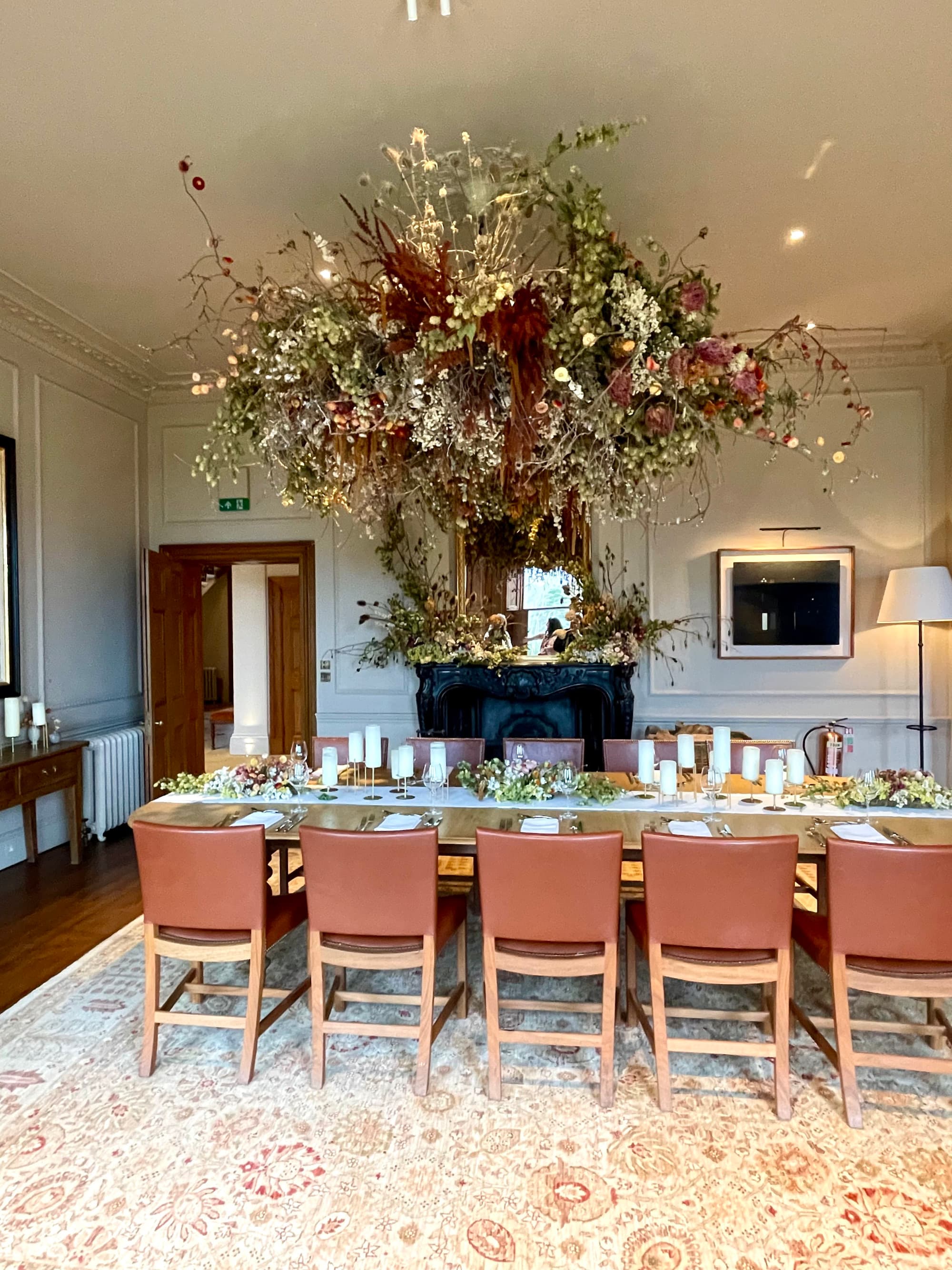 A long indoor dining table with a large floral chandelier and a pink rug