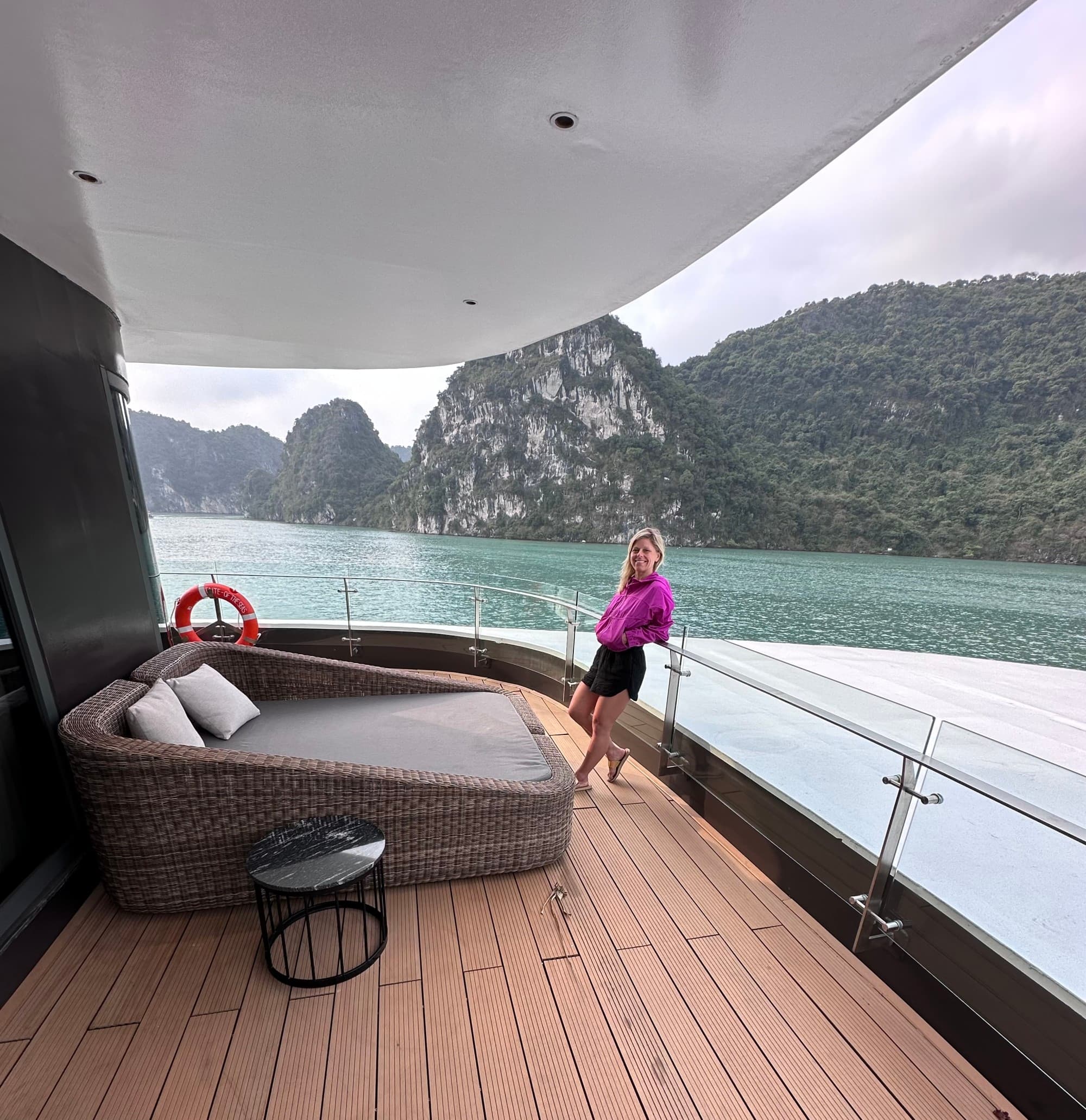 a woman in a pink jacket stands on a cruise deck