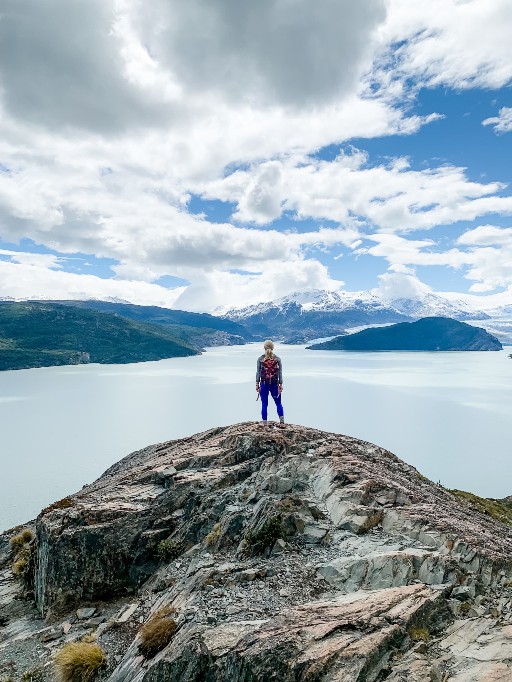 a woman stands on a rocky cliff overlooking a lake