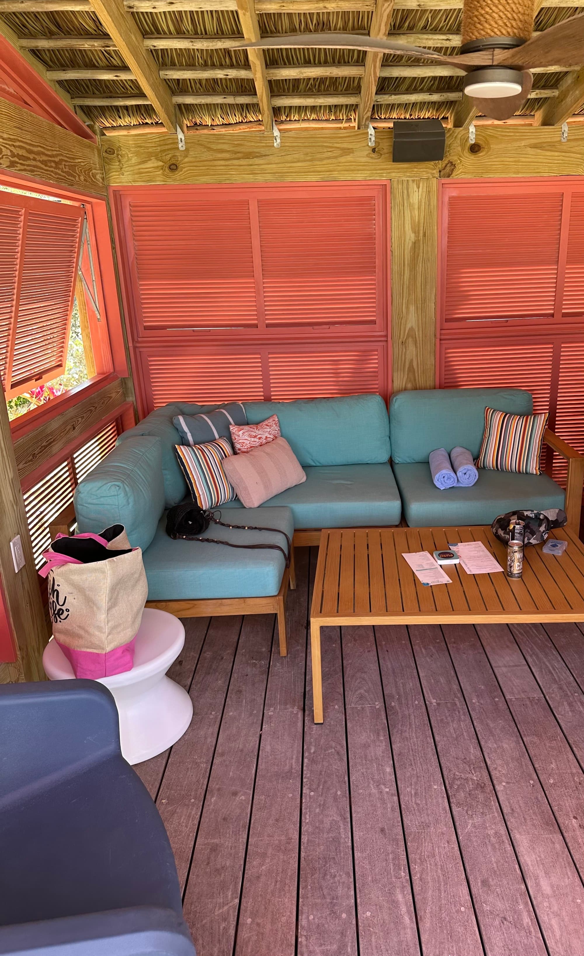 A corner of the cabana with a blue sofa, wooden coffee table and orange window shutters.