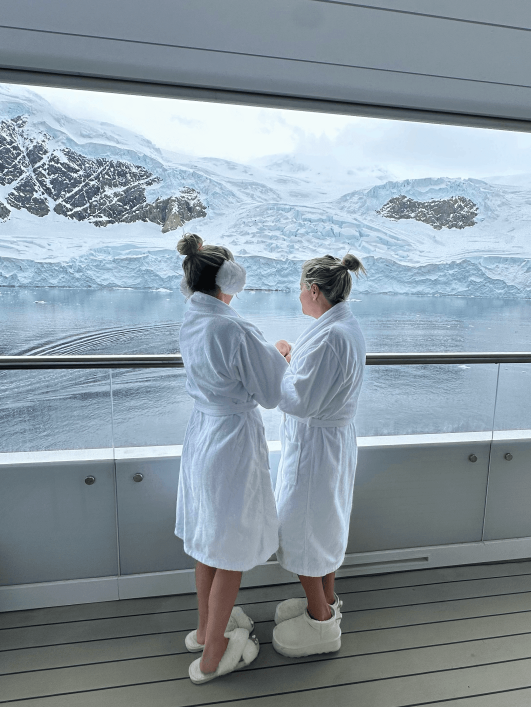 Two people in white robes and slippers standing on a ship balcony looking out to the sea