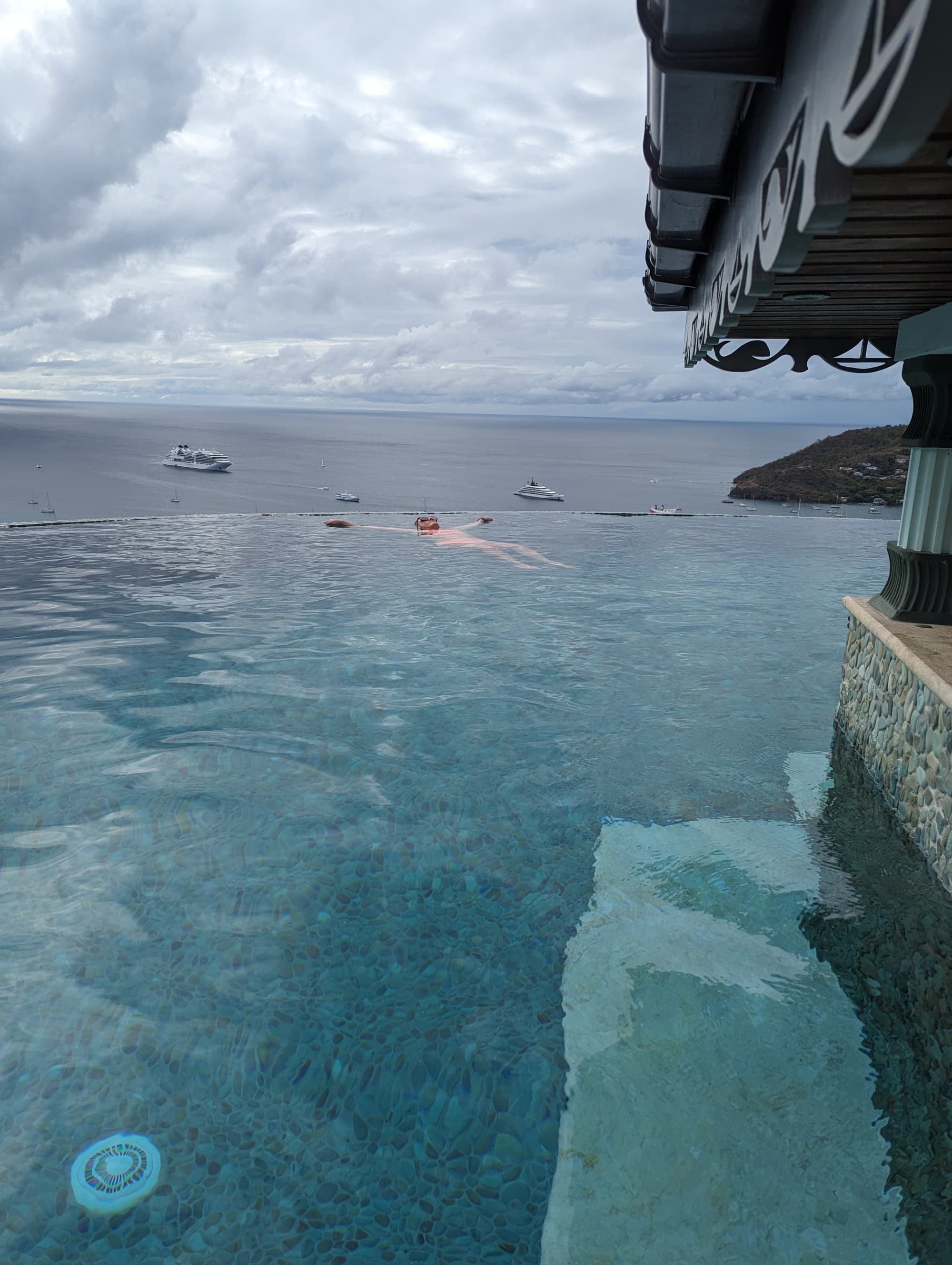 A person floating on top of the water in an infinity pool with a view of the sea in the background.