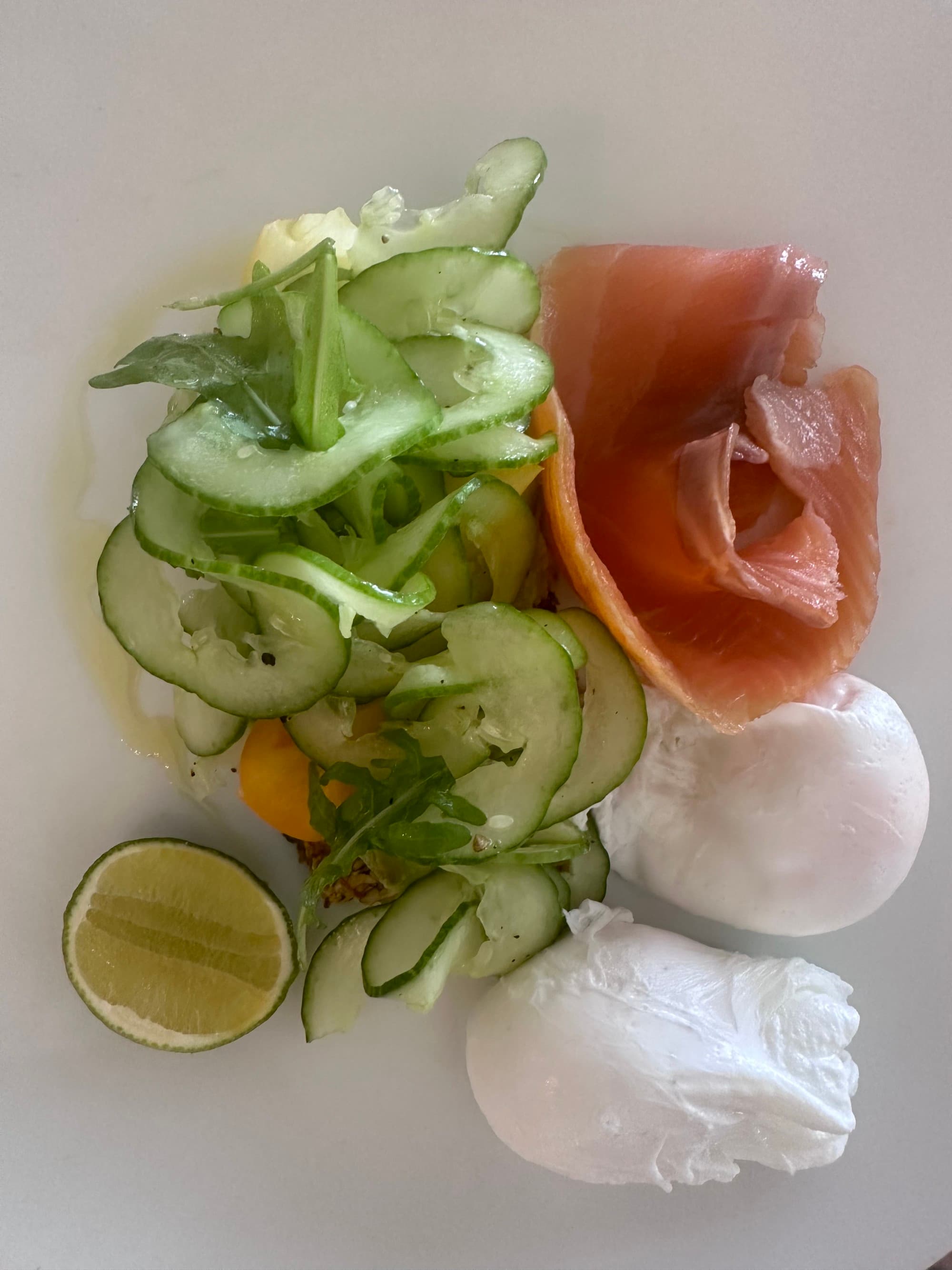 A white plate full of vegetables, limes, salmon and eggs.
