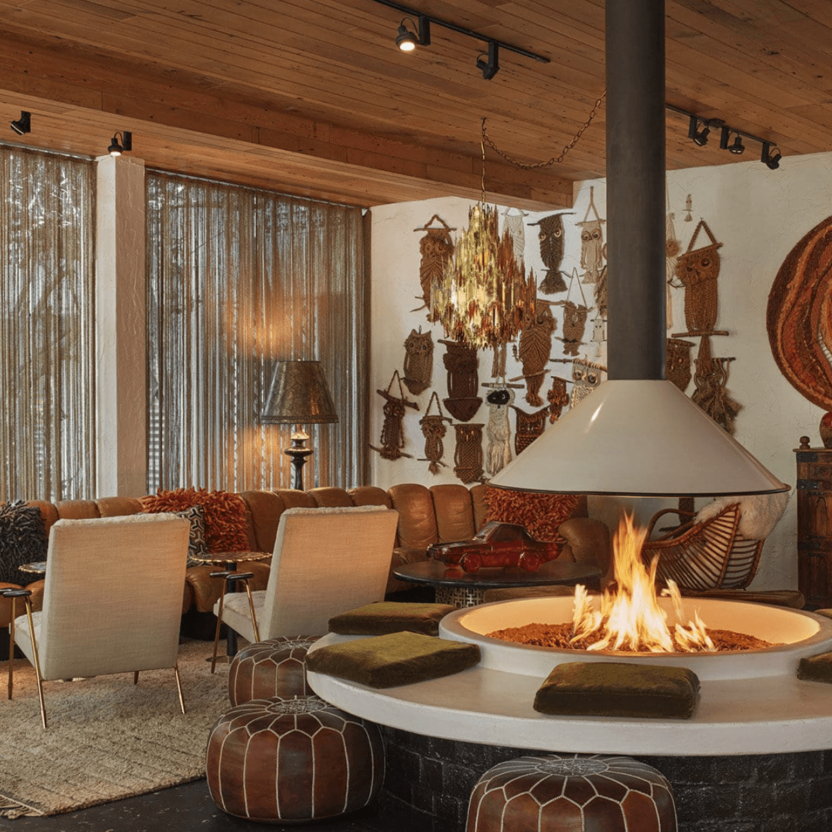 a round fire pit surrounded by leather stools in a room with eclectic artwork