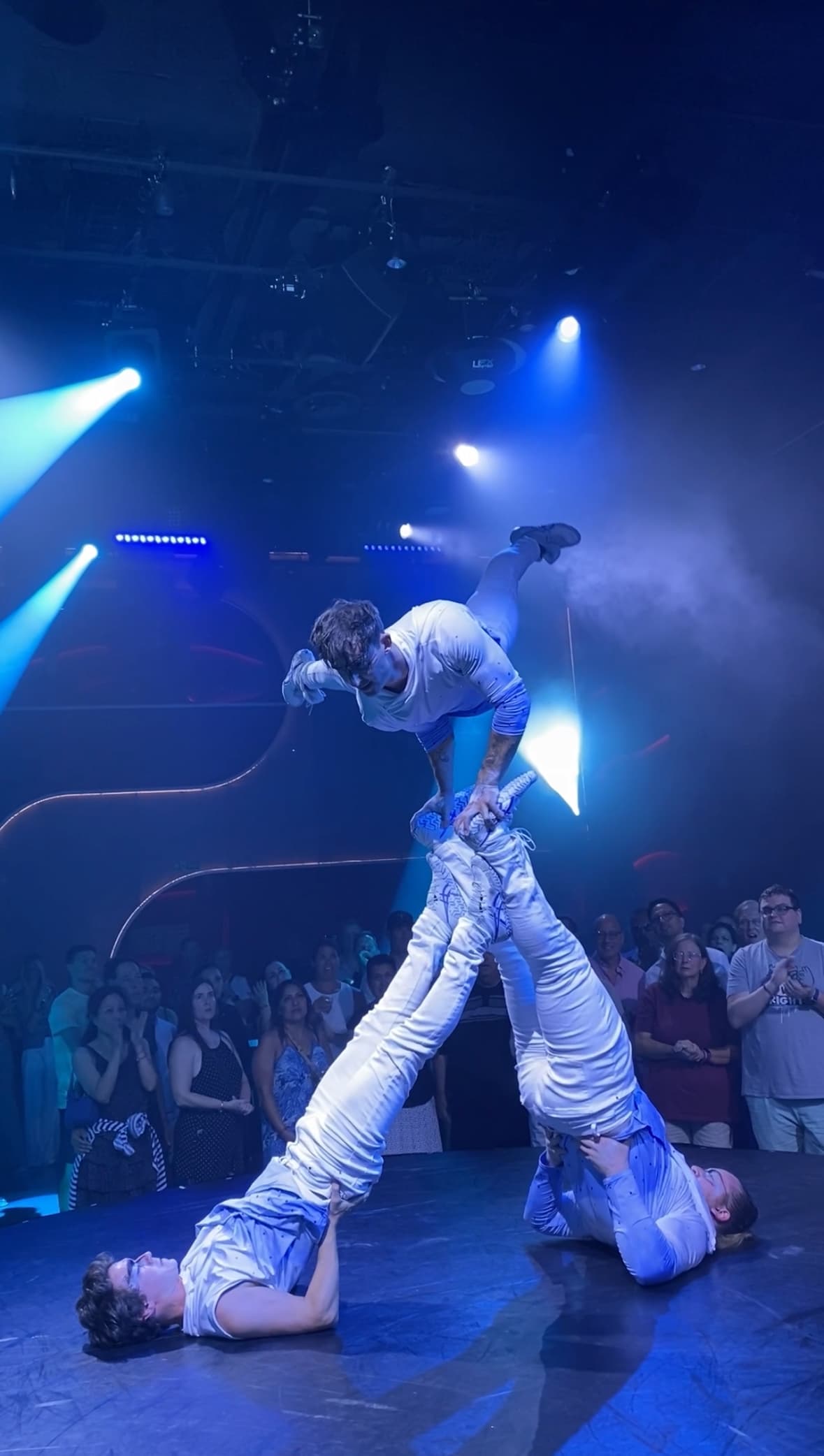 Acrobats show with three performers with blue lighting in a dark room and audience