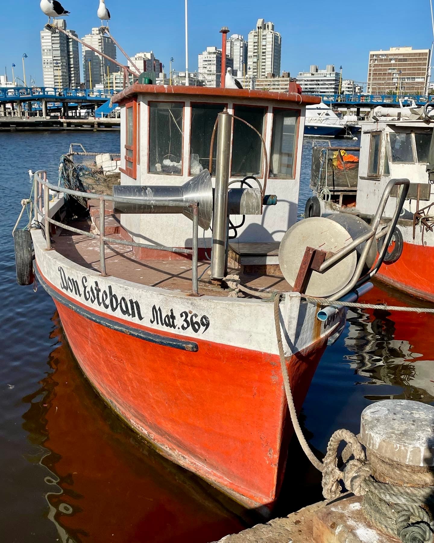A red and white fisherman boat tied to a dock in a harbor.