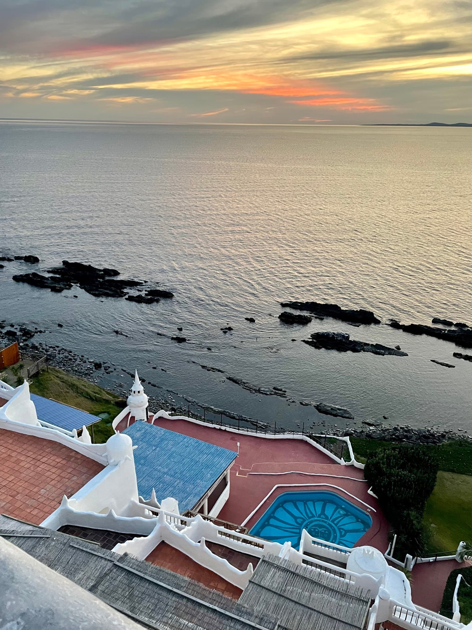 A sliver of an orange sky above the sea with building rooftops in the near distance.