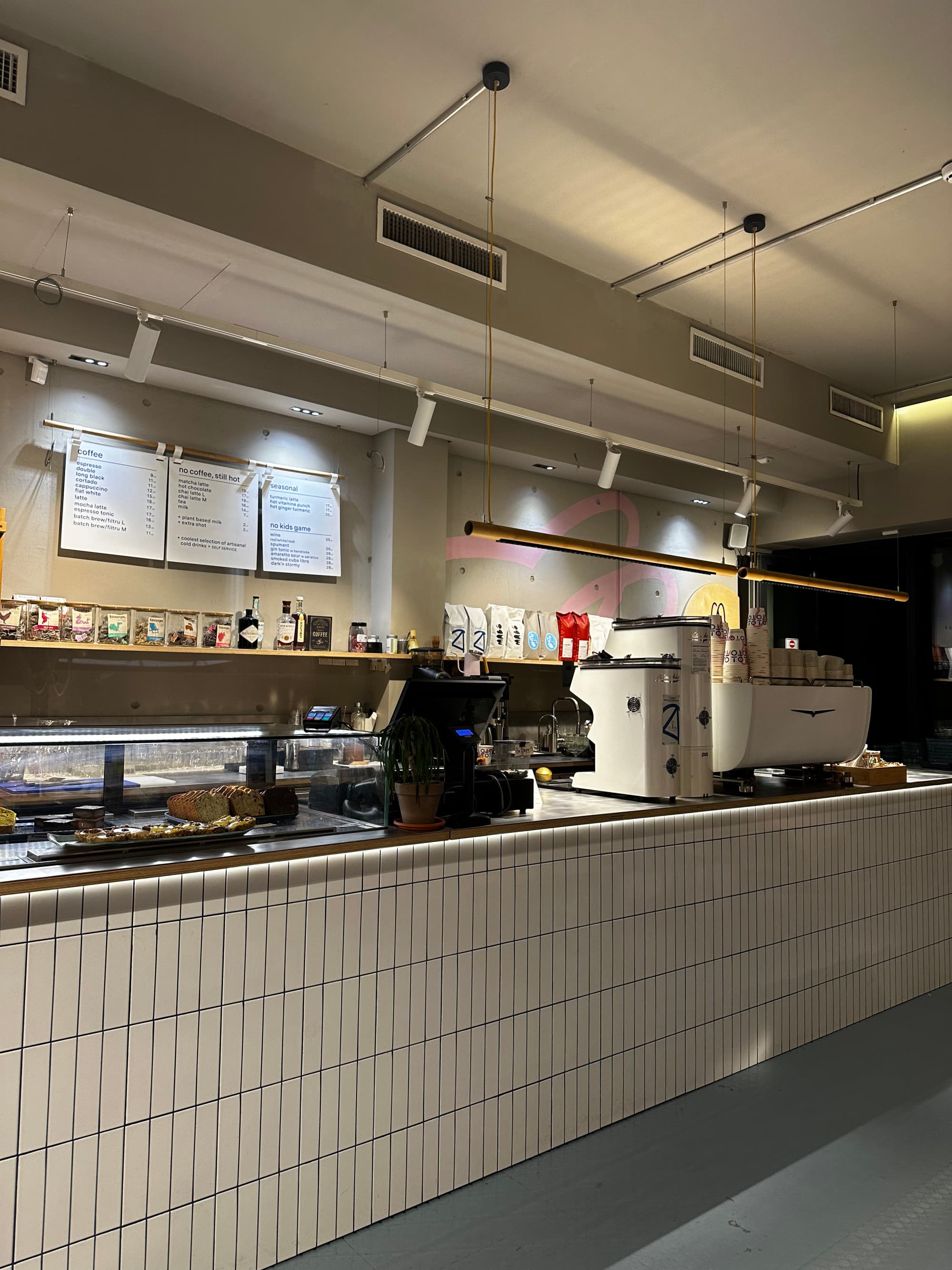 A view of a coffee bar with white subway tiling, a menu on the wall and coffee machines.