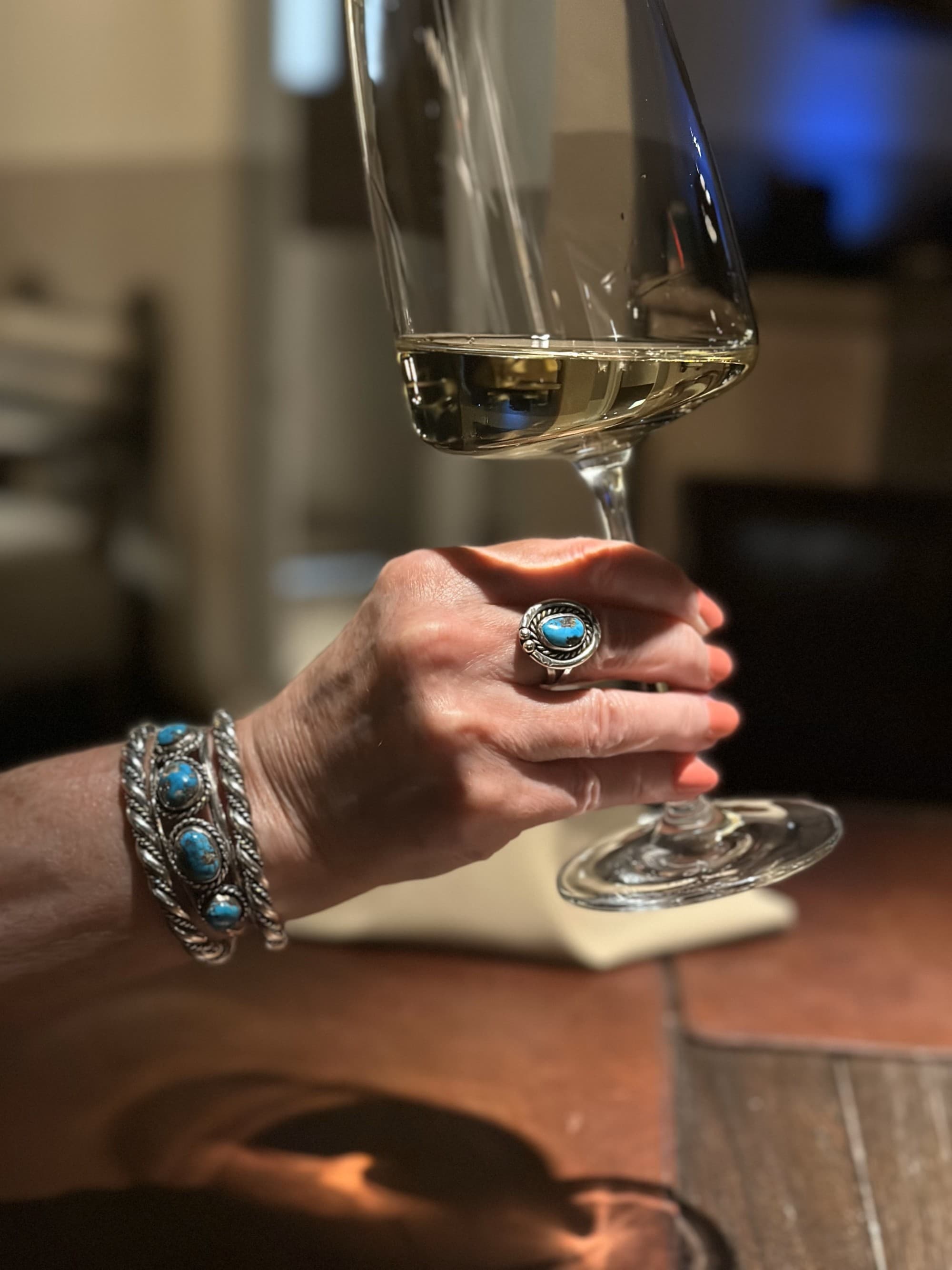 A close-up shot of a woman's hand raising a glass filled with white wine.