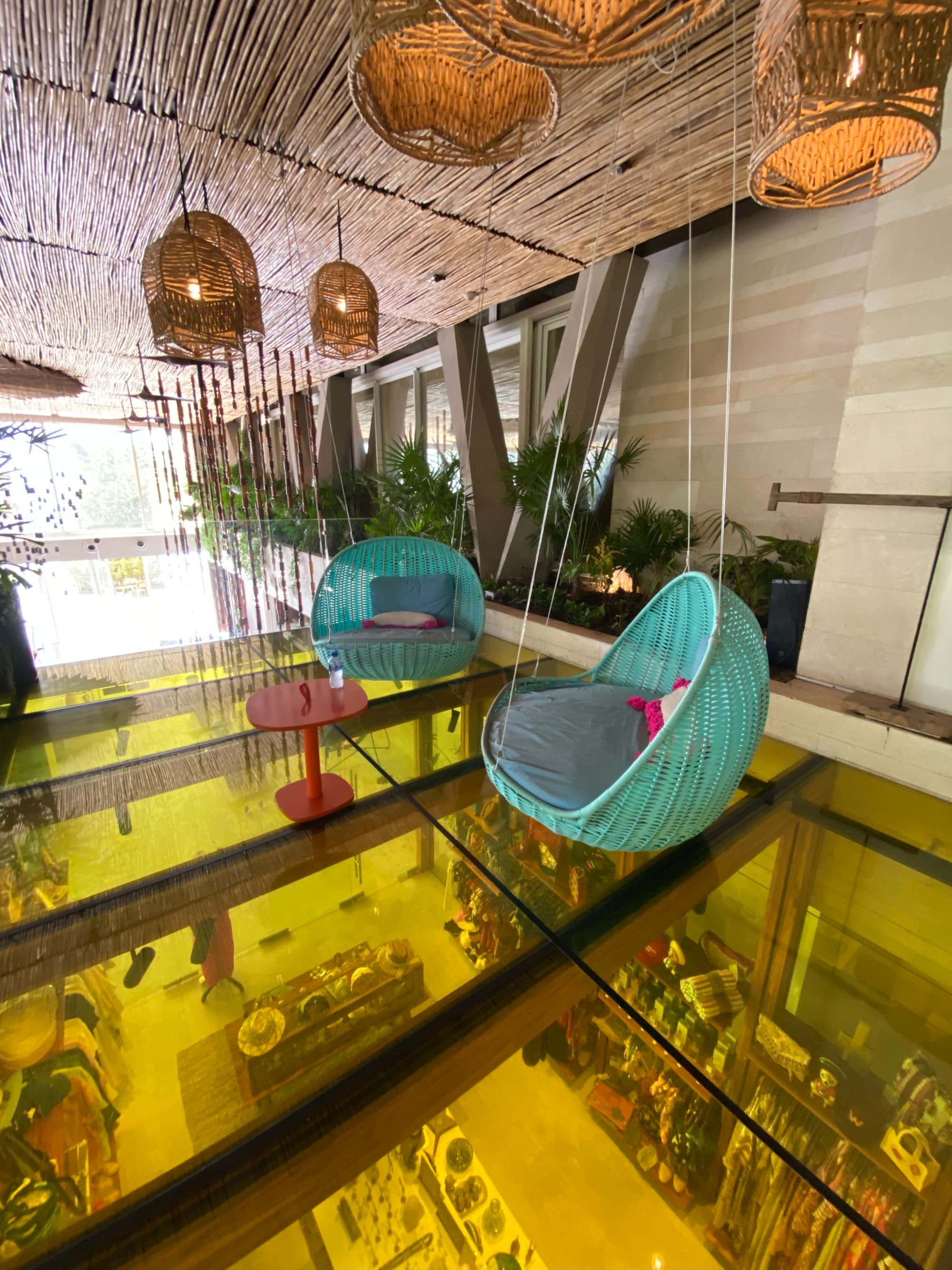 A colorful lobby of a hotel with with yellow glass floor and blue hanging chairs