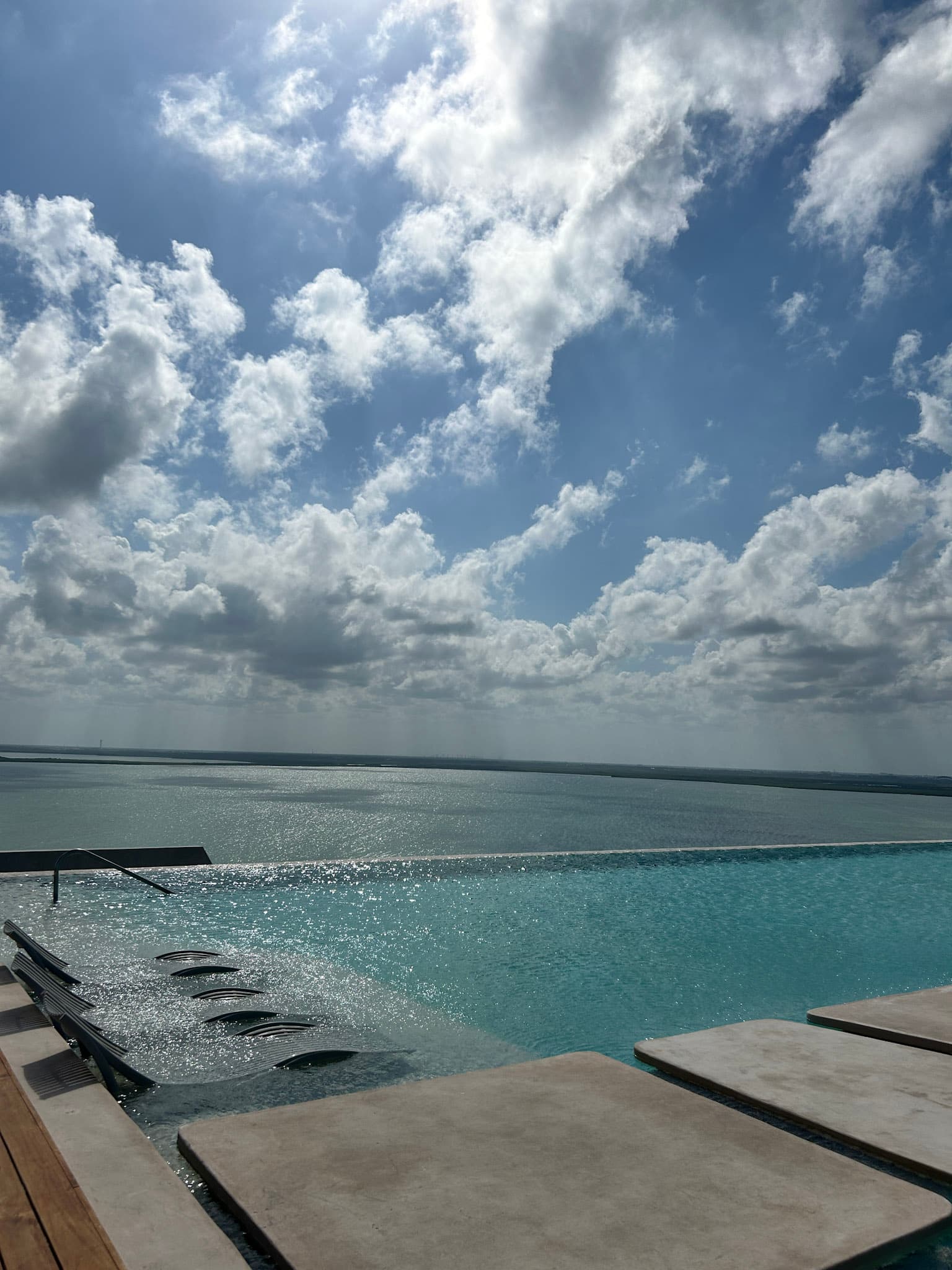 An infinity pool with lounge chairs in the water, with a view of the sea and sky in the background.