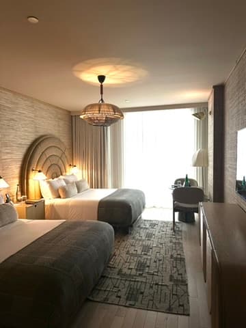 Inside the Santa Monica Proper Hotel, with two double beds, muted tones, a desk, and glass door leading to a balcony.