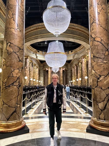Travel advisor standing in between two grand, marble columns inside of a luxurious lobby, with crystal chandeliers above him.