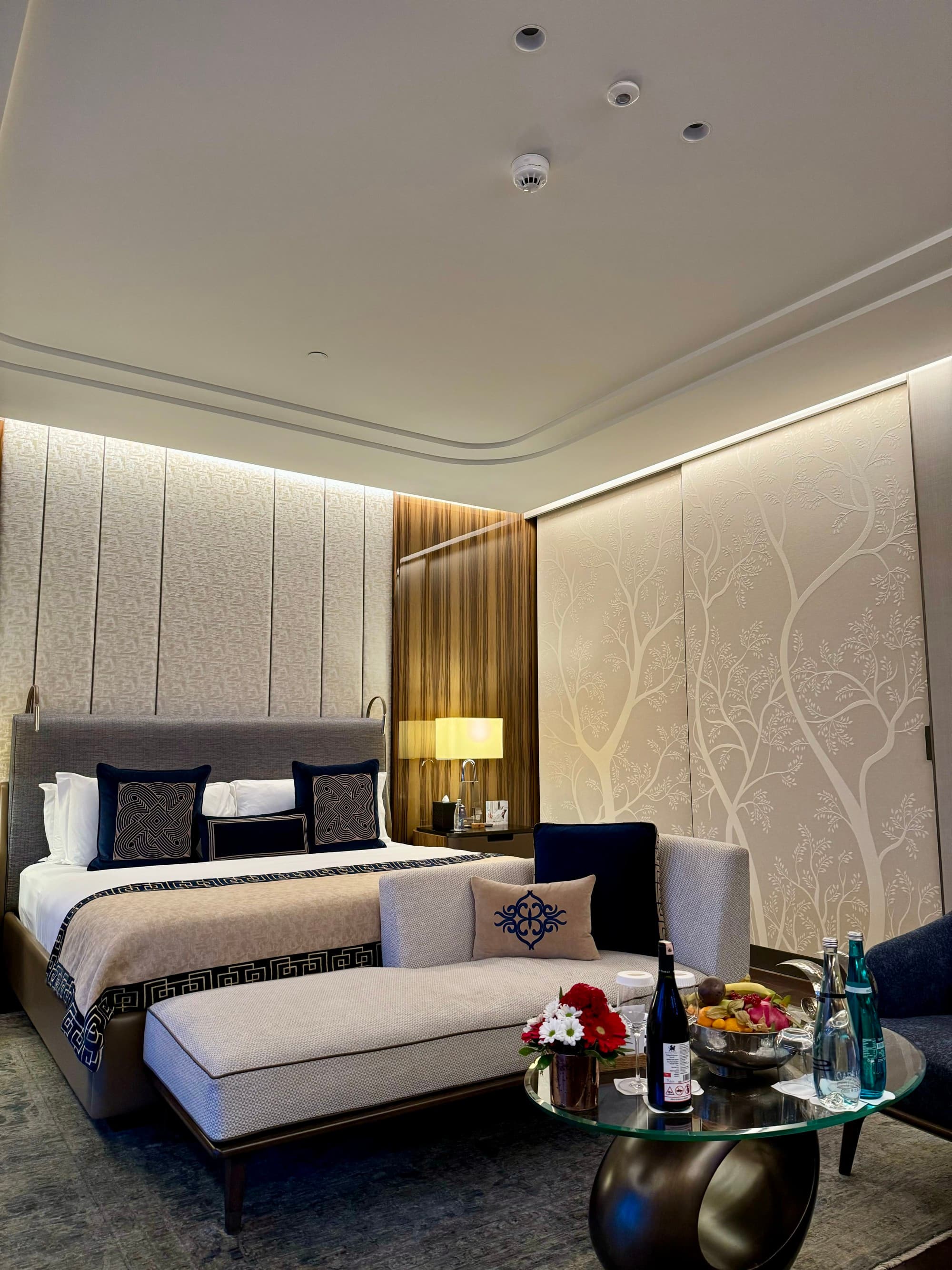 A queen-sized bed room with a small round table topped with welcome treats.