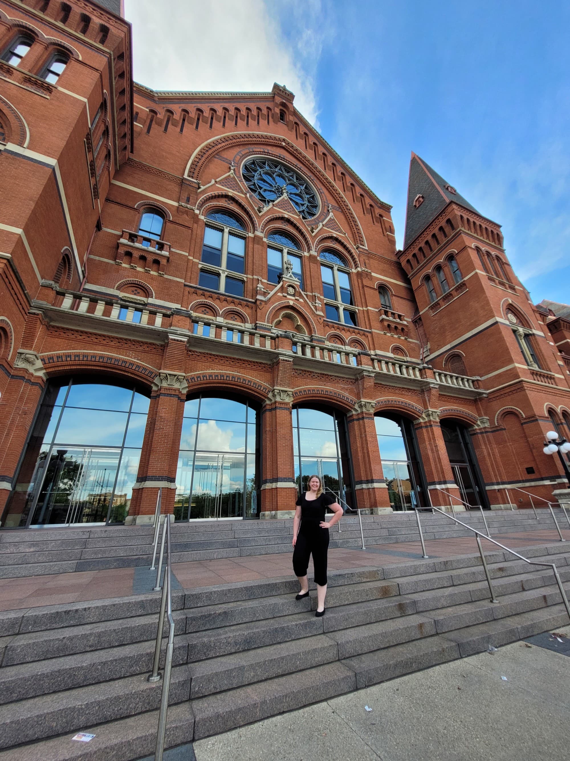 A low-angled photo of a person standing on steps in front of a large, red-brick building