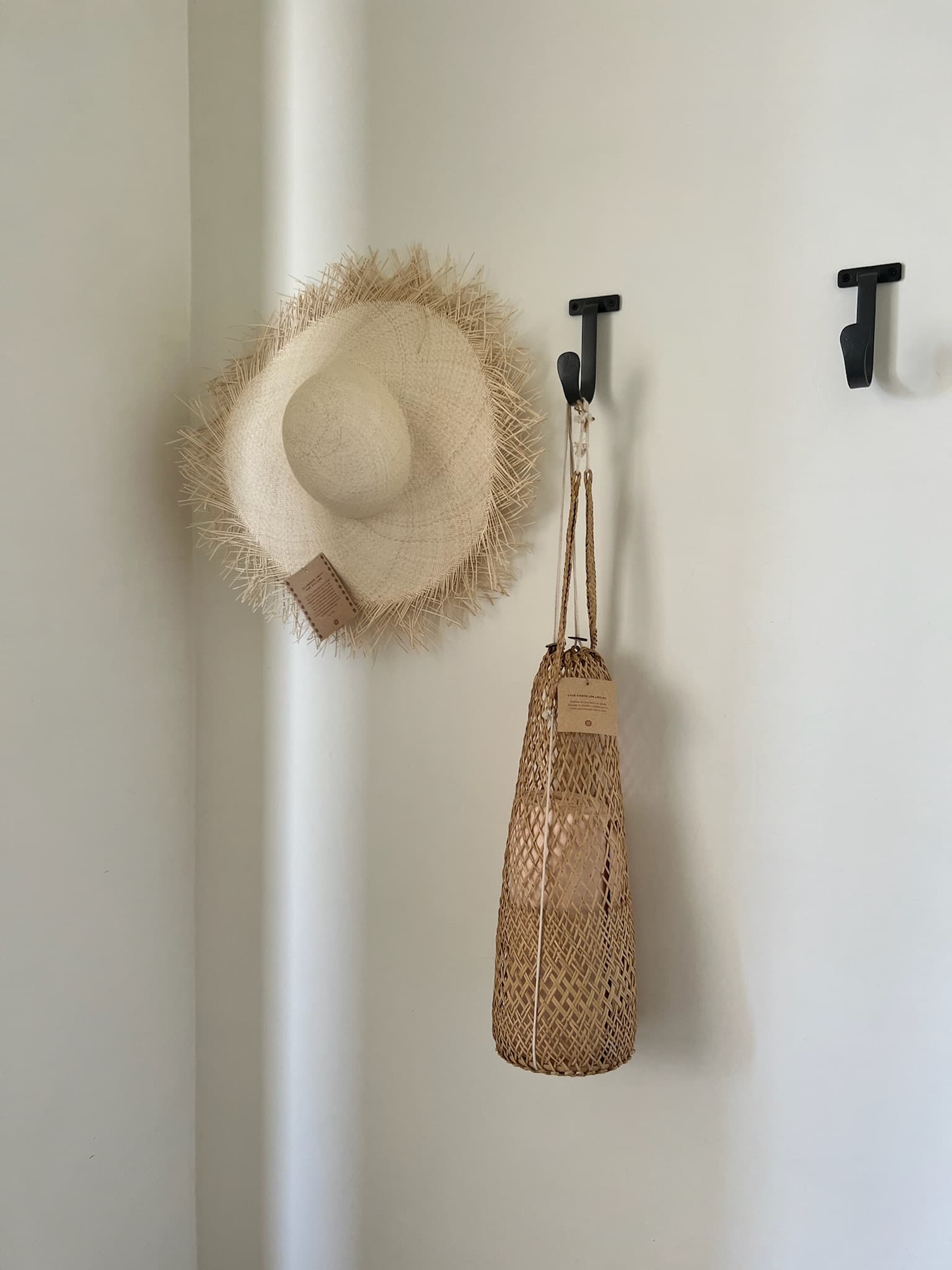 A beige beach hat and bag hanging from a black hook against a white wall.