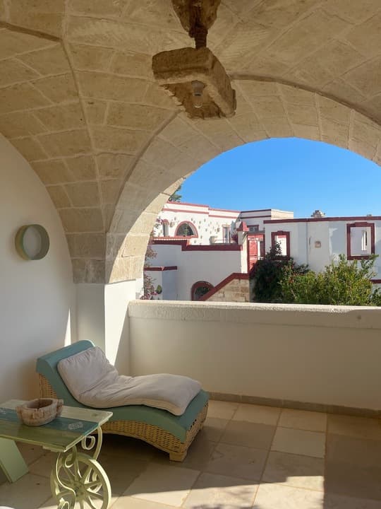 A curved lounge chair placed on a covered balcony with a view of the villa in the background.