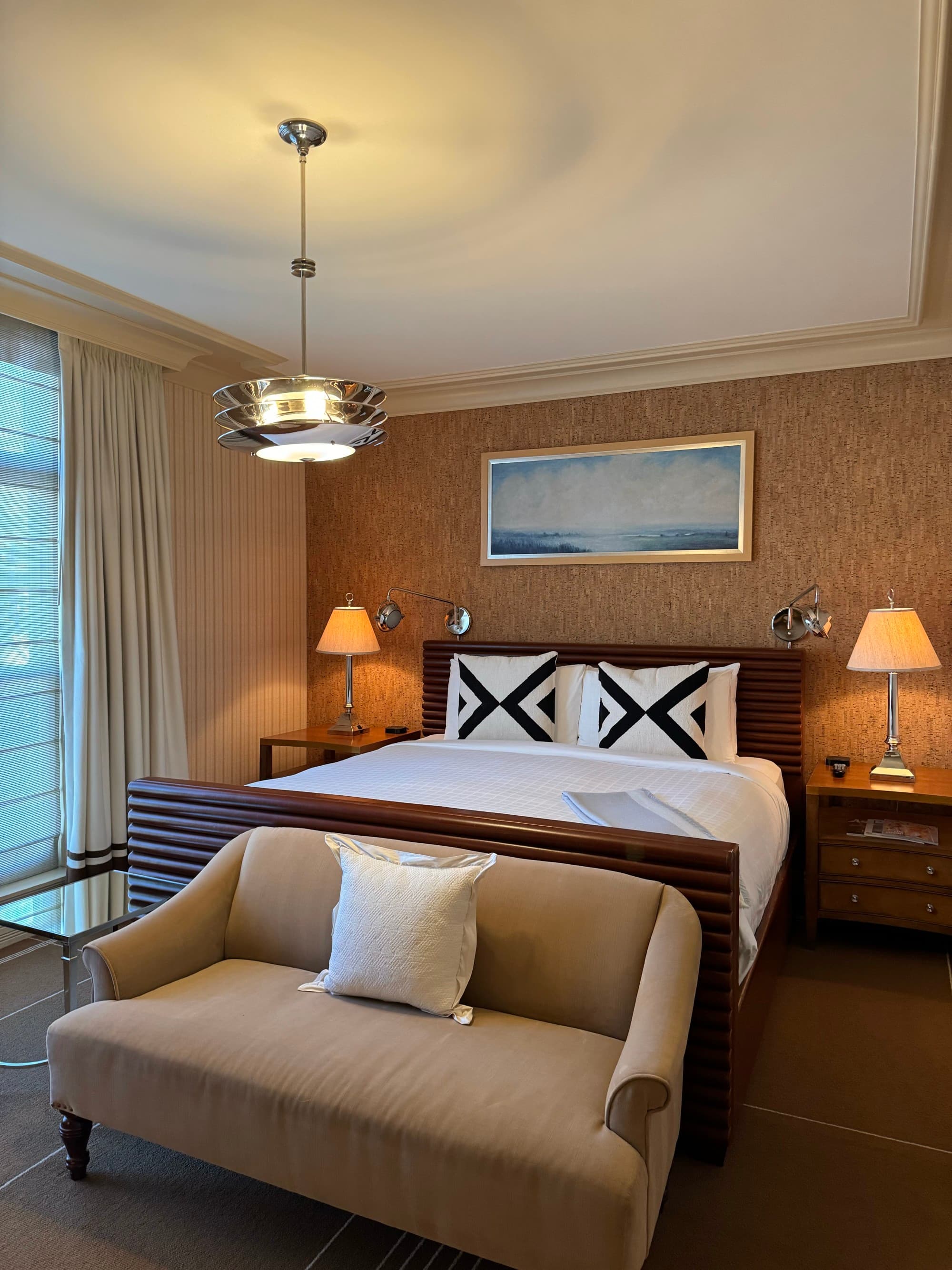 Inside another hotel bedroom with muted colors for the decor, a big bed and beige loveseat.