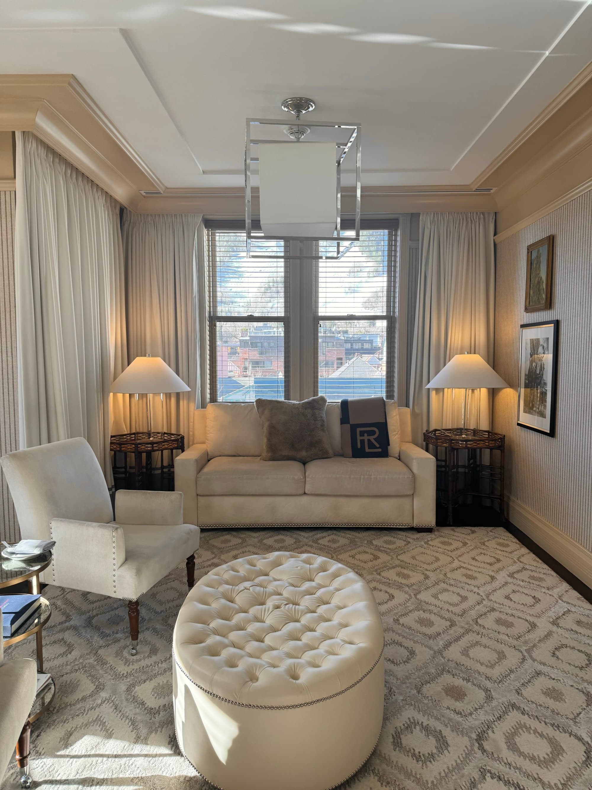 A sitting area inside one of the hotel rooms, with soft, white furniture and rug, with a subtle yet elegant design.
