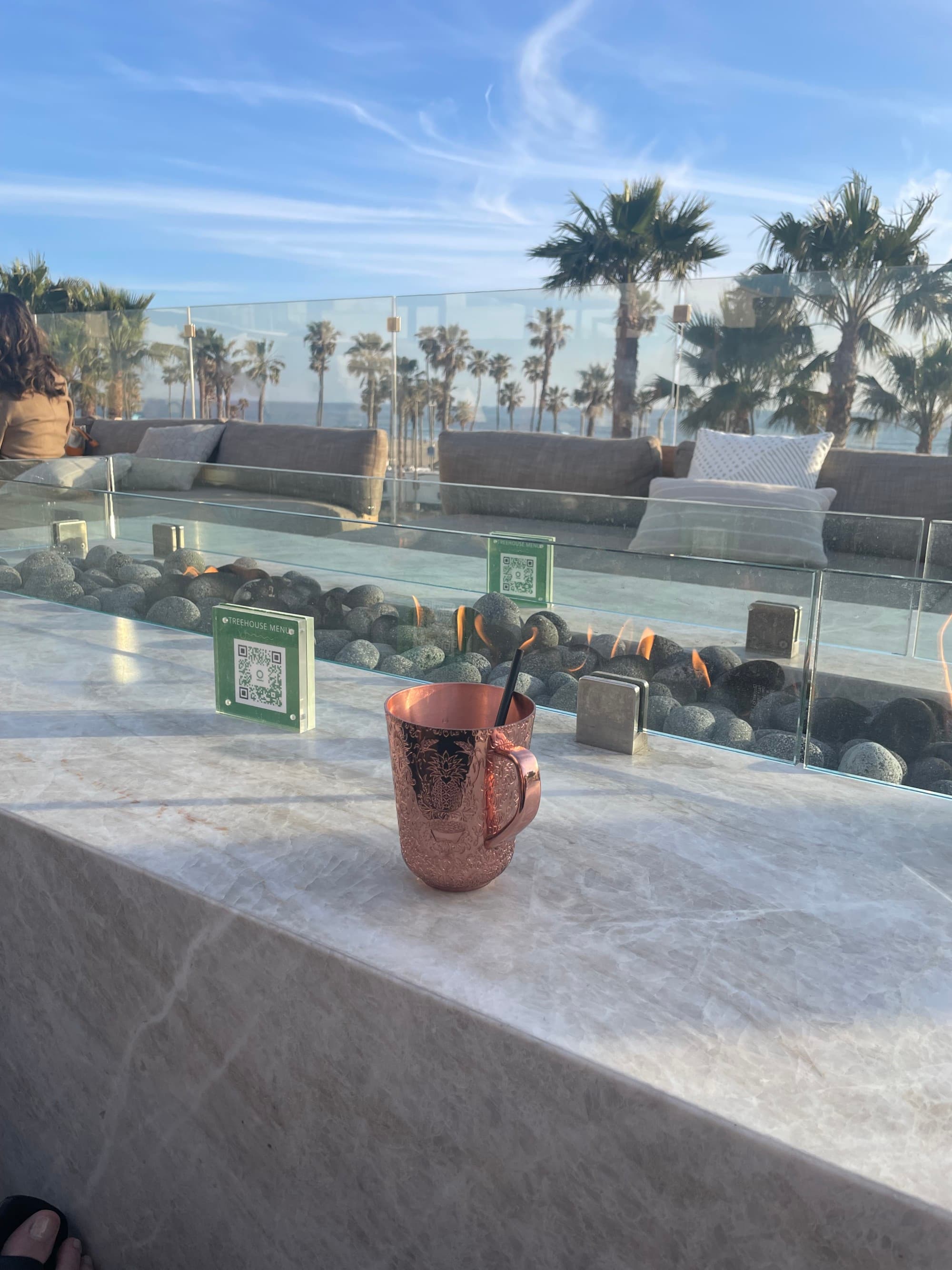 A copper cup on a marble balcony with palm trees in the background at Treehouse Rooftop Bar - Michelle Roe