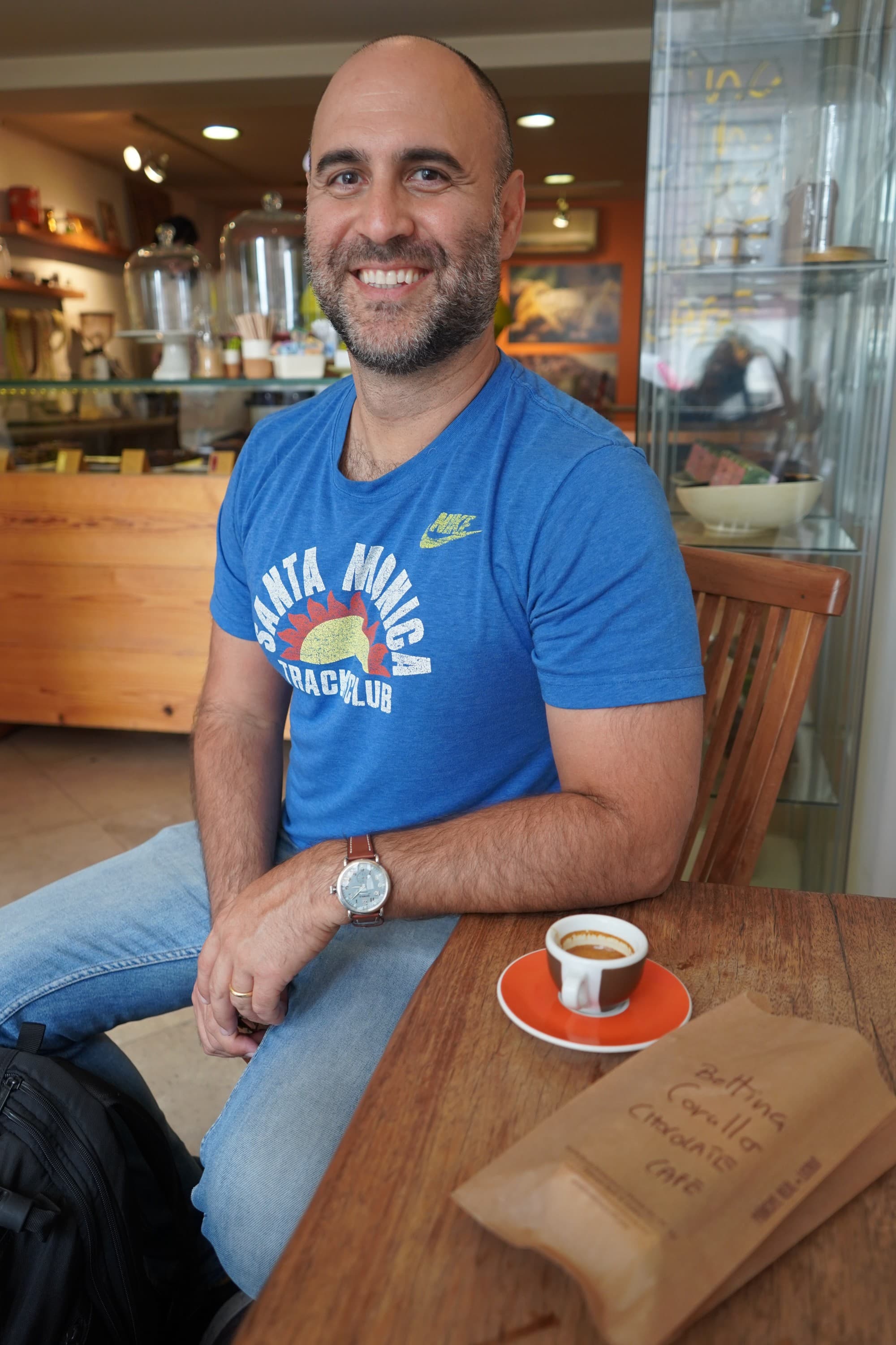 a man in a blue shirt sits at a wooden table with a small cup of espresso