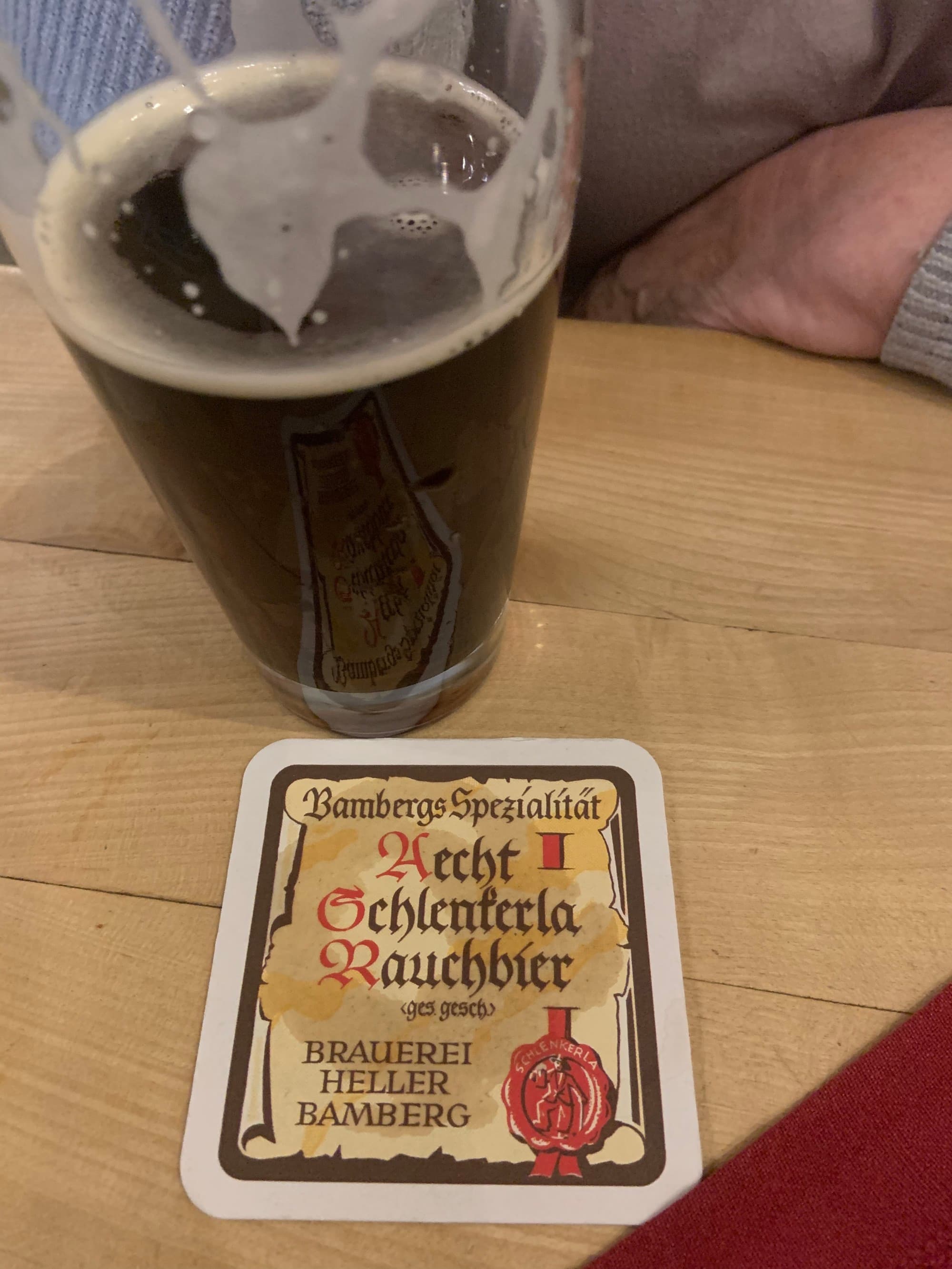 A glass of dark beer on a wooden table with a coaster.