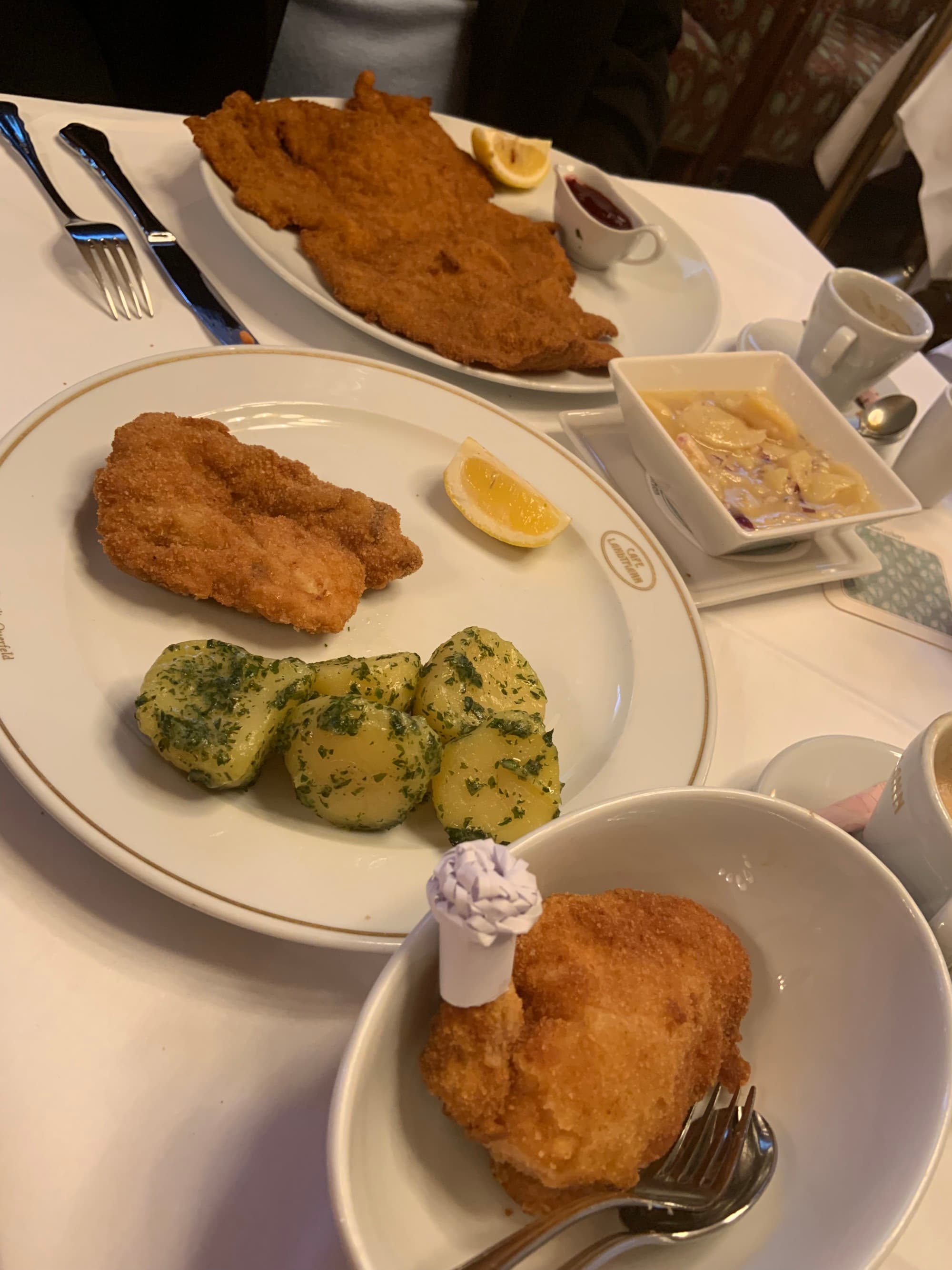 Several plates of schnitzel served at a restaurant on white plates and a white tablecloth.