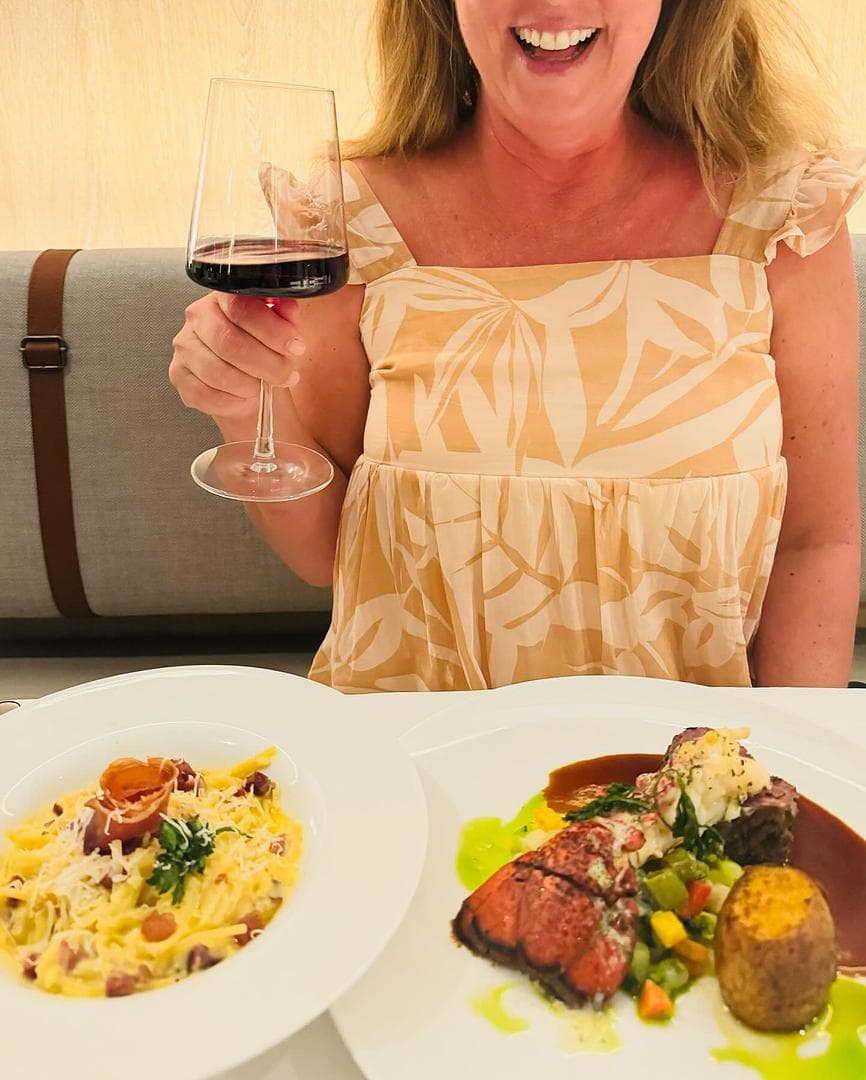 A woman holding a glass of wine with two dishes in front of her at a restaurant.