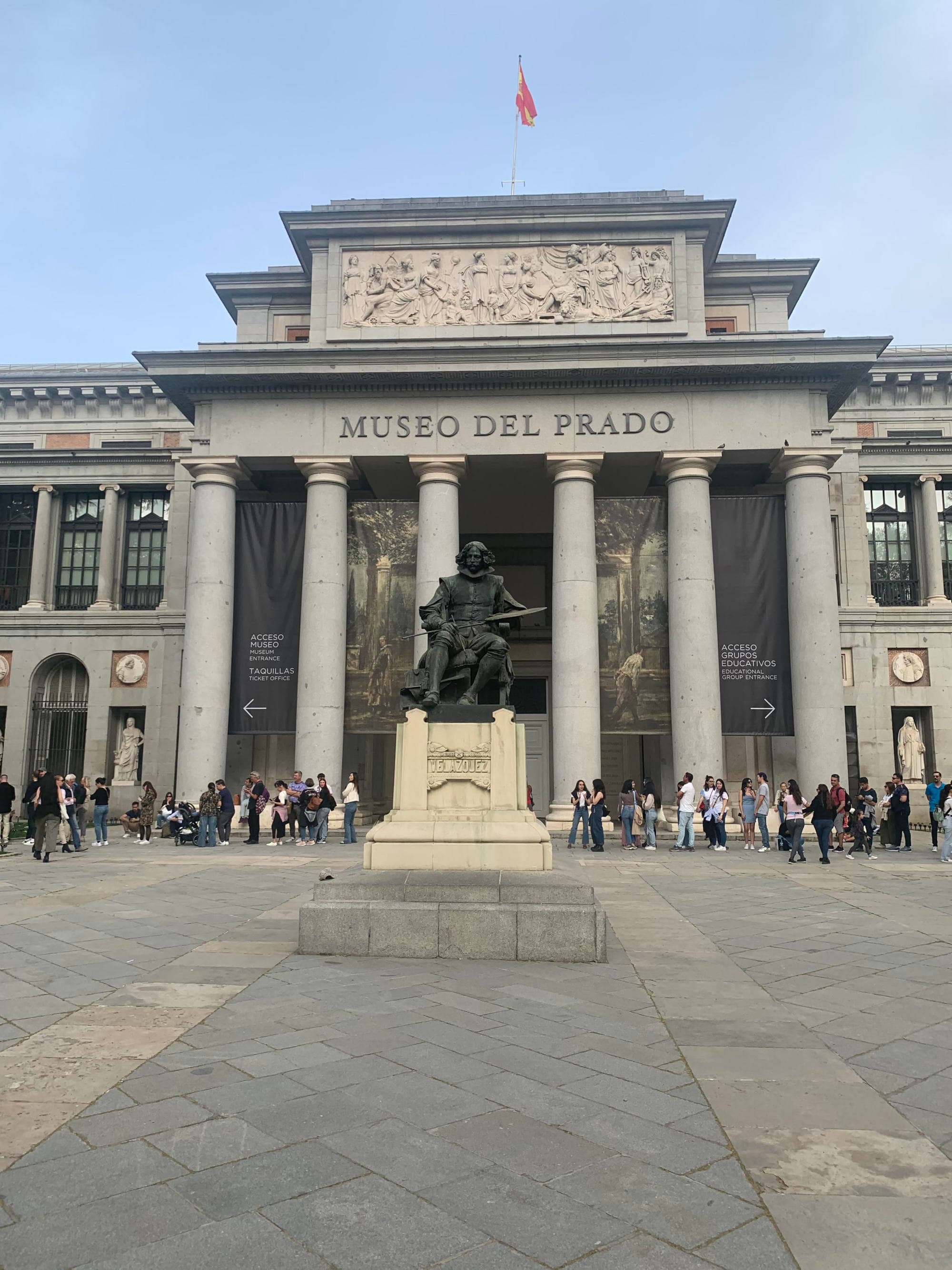 Exterior of the Museo Del Prado, with Grecian columns and a status carved from dark rock.